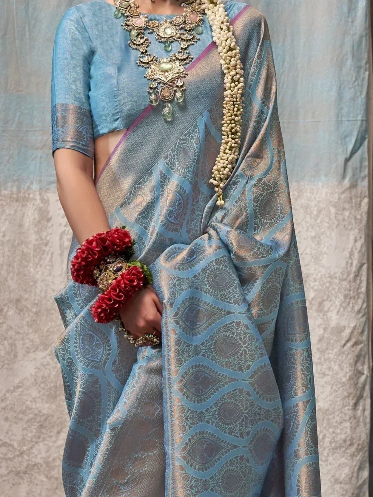 Blue designer saree with gold paisley print, ethnic jewelry, and floral wristband for Indian occasions