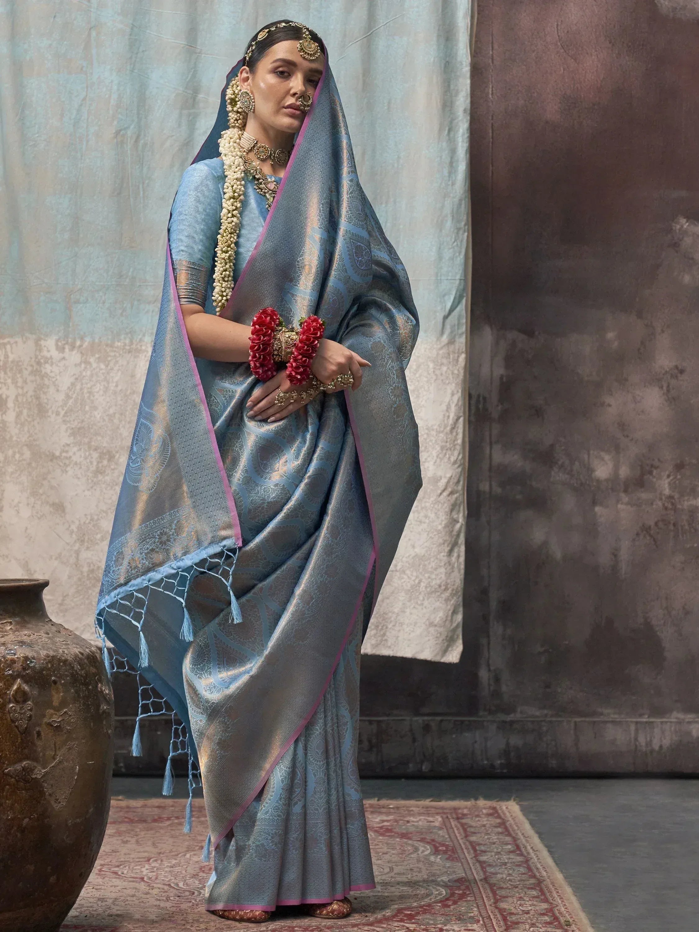 Blue designer saree with gold paisley print, pink border, and tassels, styled with traditional jewelry for Indian ethnic wear