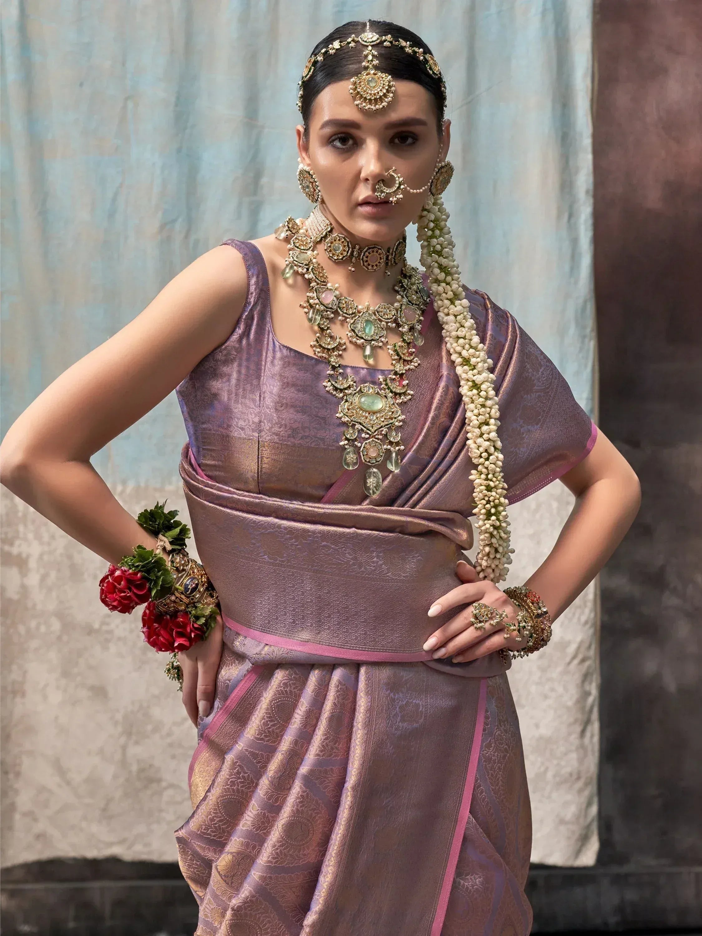 Elegant woman in purple designer saree with gold jewelry and floral accessories, showcasing Indian ethnic wear.