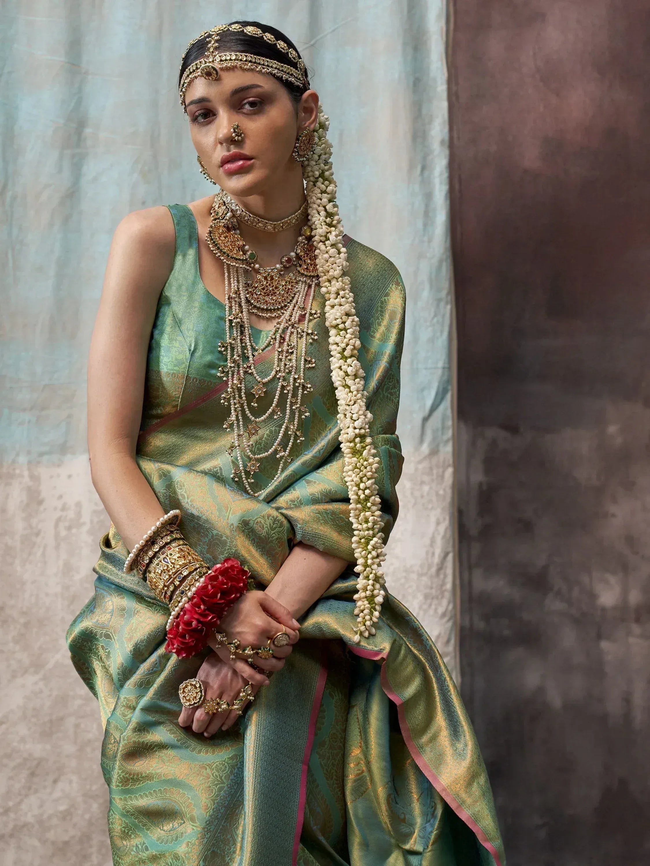Woman in green and gold designer saree with traditional Indian bridal jewelry and floral gajra