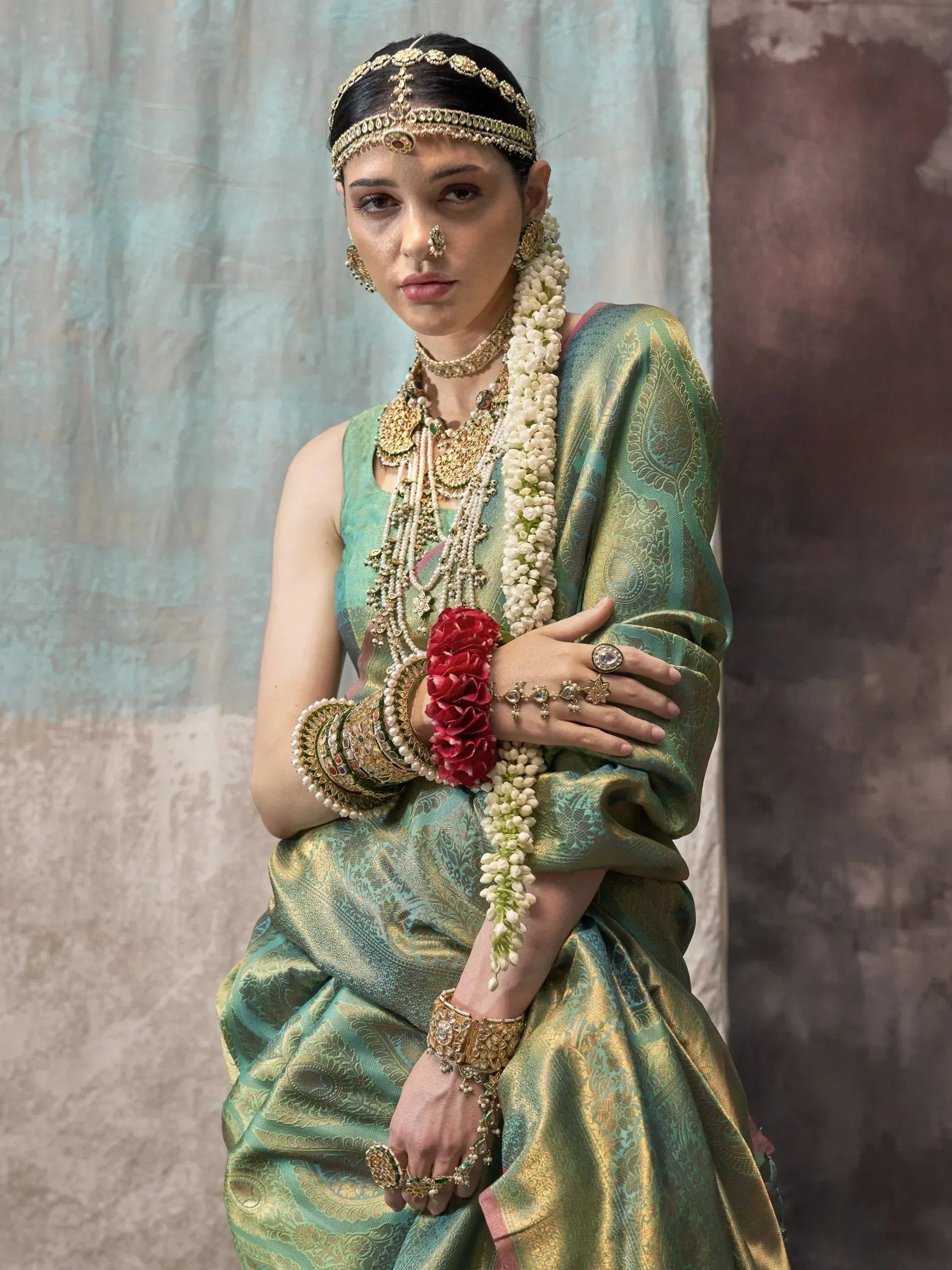 Woman in traditional Indian green and gold saree with heavy jewelry and floral garland