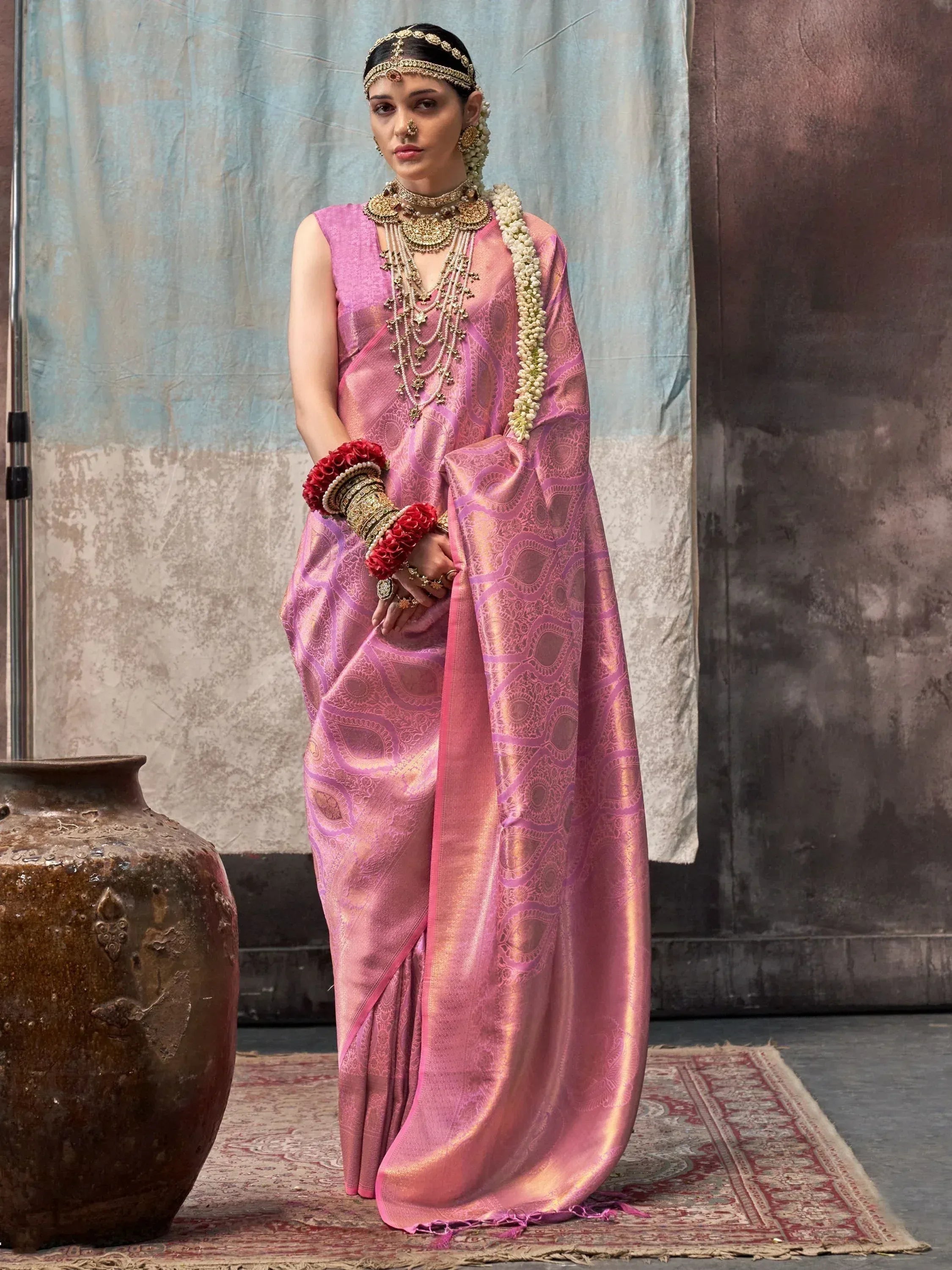Pink designer saree with gold embroidery, traditional Indian bridal jewelry, and floral garland for wedding wear