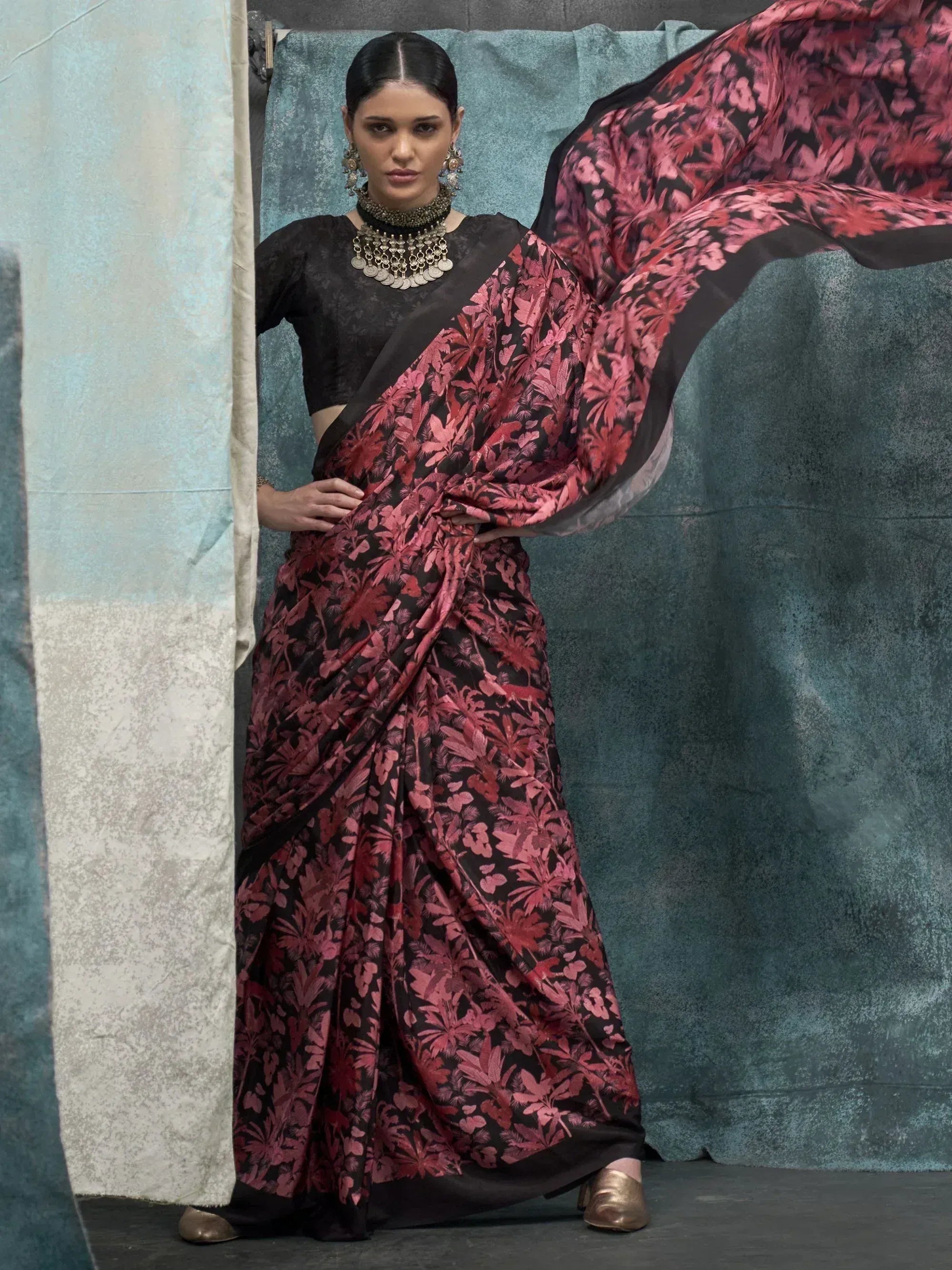 Woman in black and pink floral print saree with matching blouse, styled with traditional jewelry for ethnic wear.