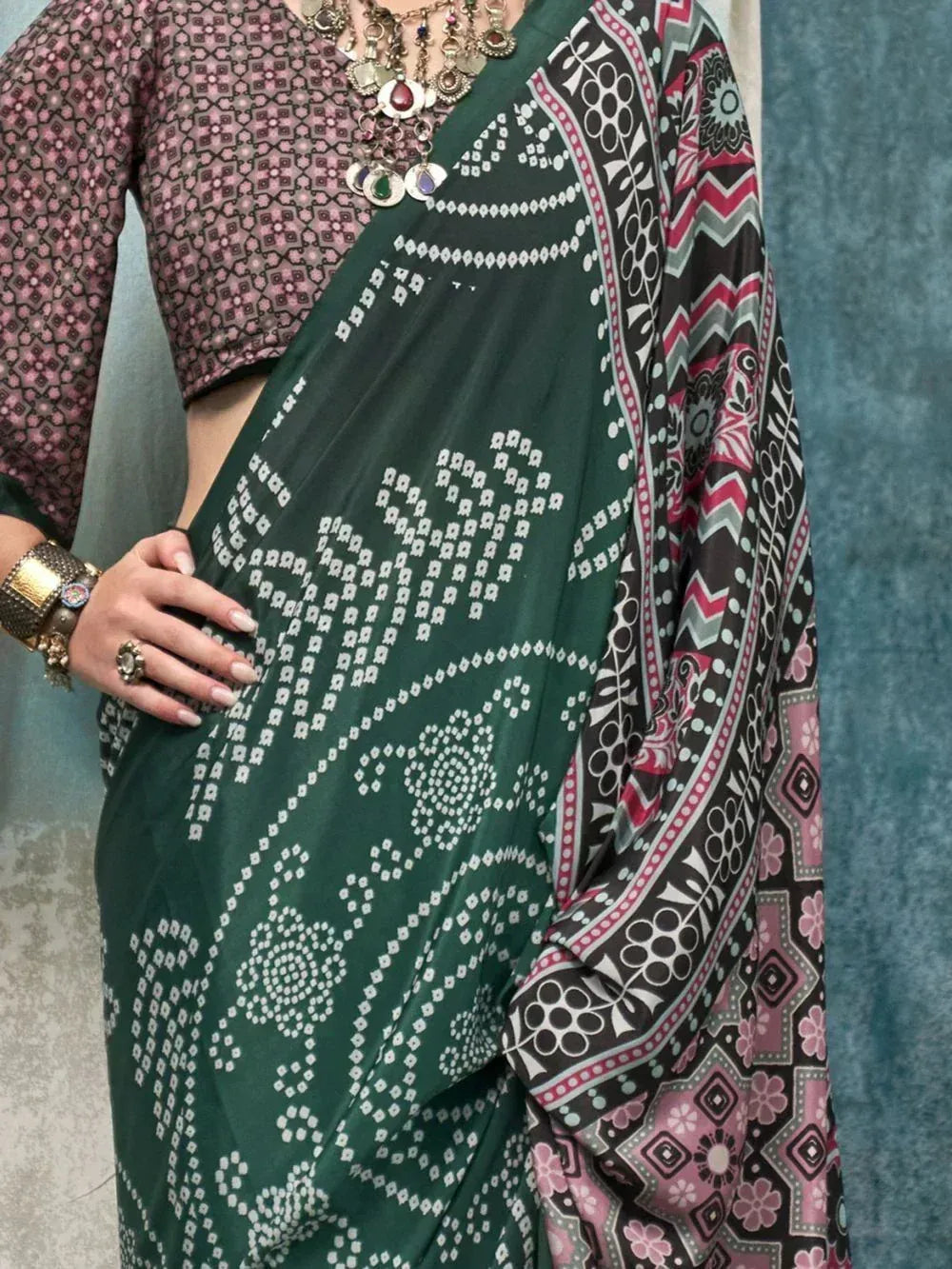 Green printed saree with pink and black border, paired with patterned blouse and ethnic jewelry