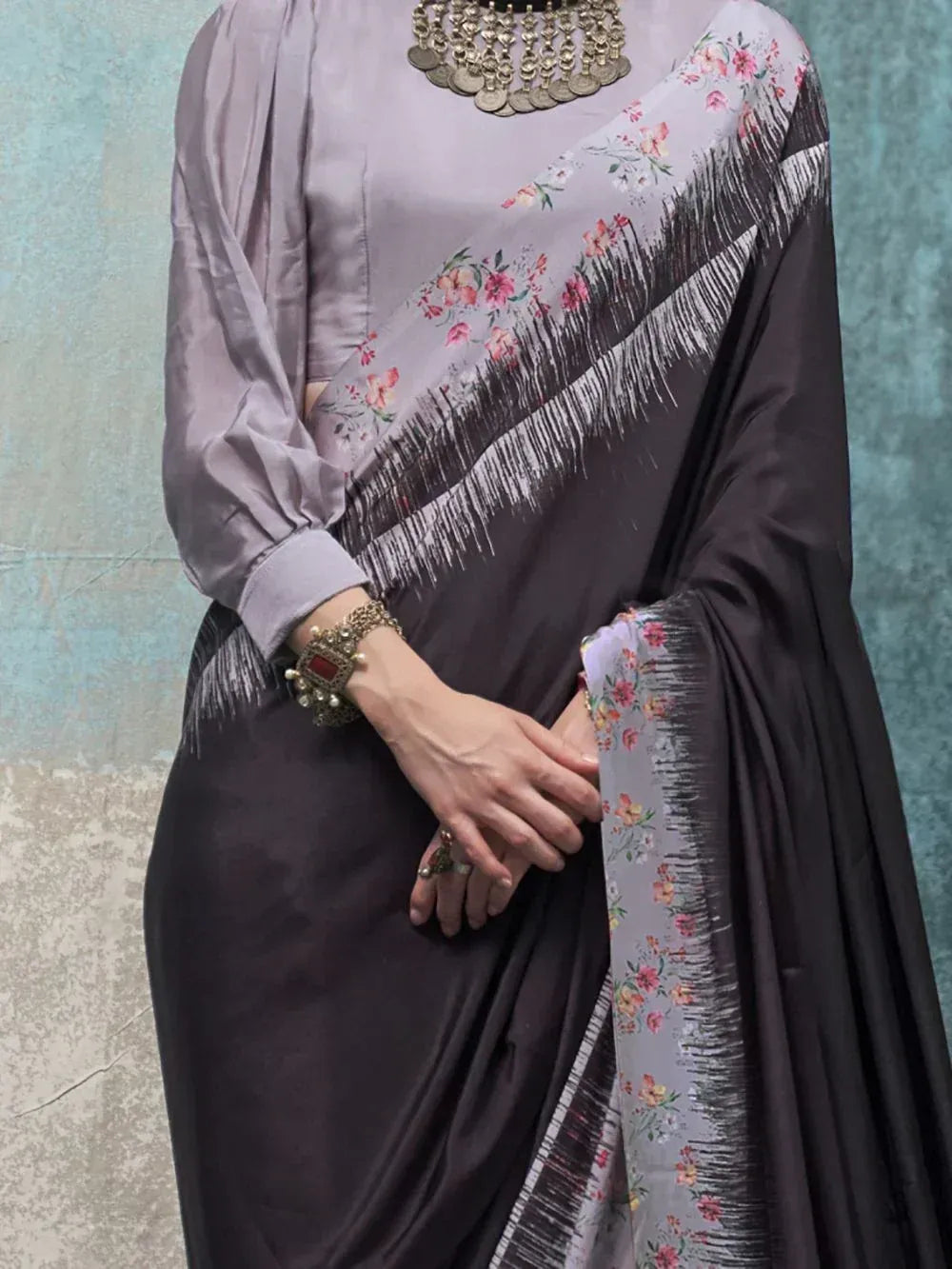 Elegant grey floral saree with black border and fringe, paired with matching blouse and ethnic jewelry