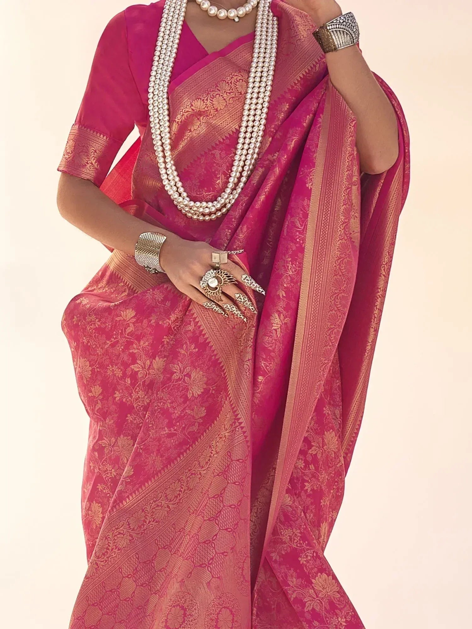 Pink designer saree with gold floral patterns, paired with pearl necklace and ethnic jewelry