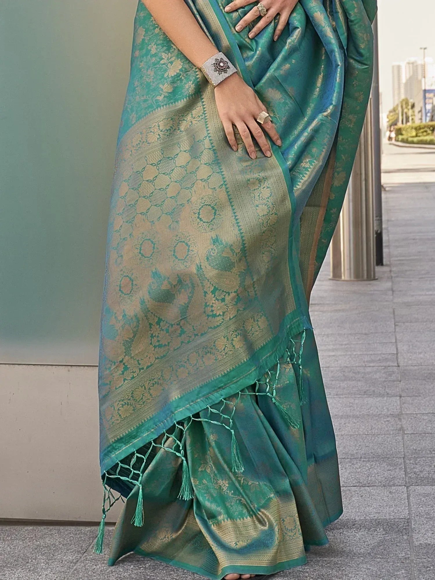 Teal green designer saree with gold floral and paisley motifs, tassels, and ethnic weave pattern
