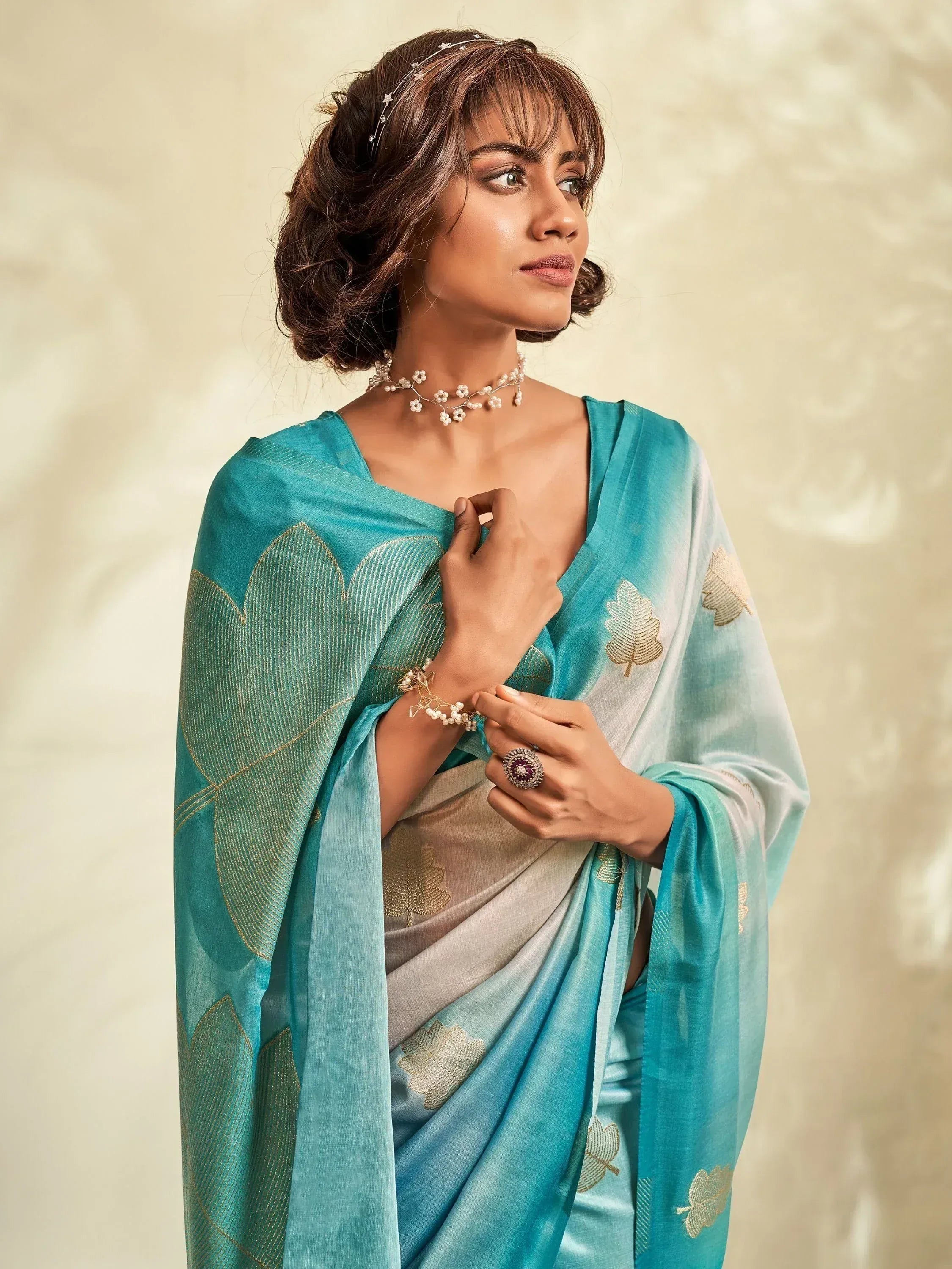 Woman in elegant turquoise saree with gold leaf embroidery, styled with floral jewelry for Indian ethnic wear