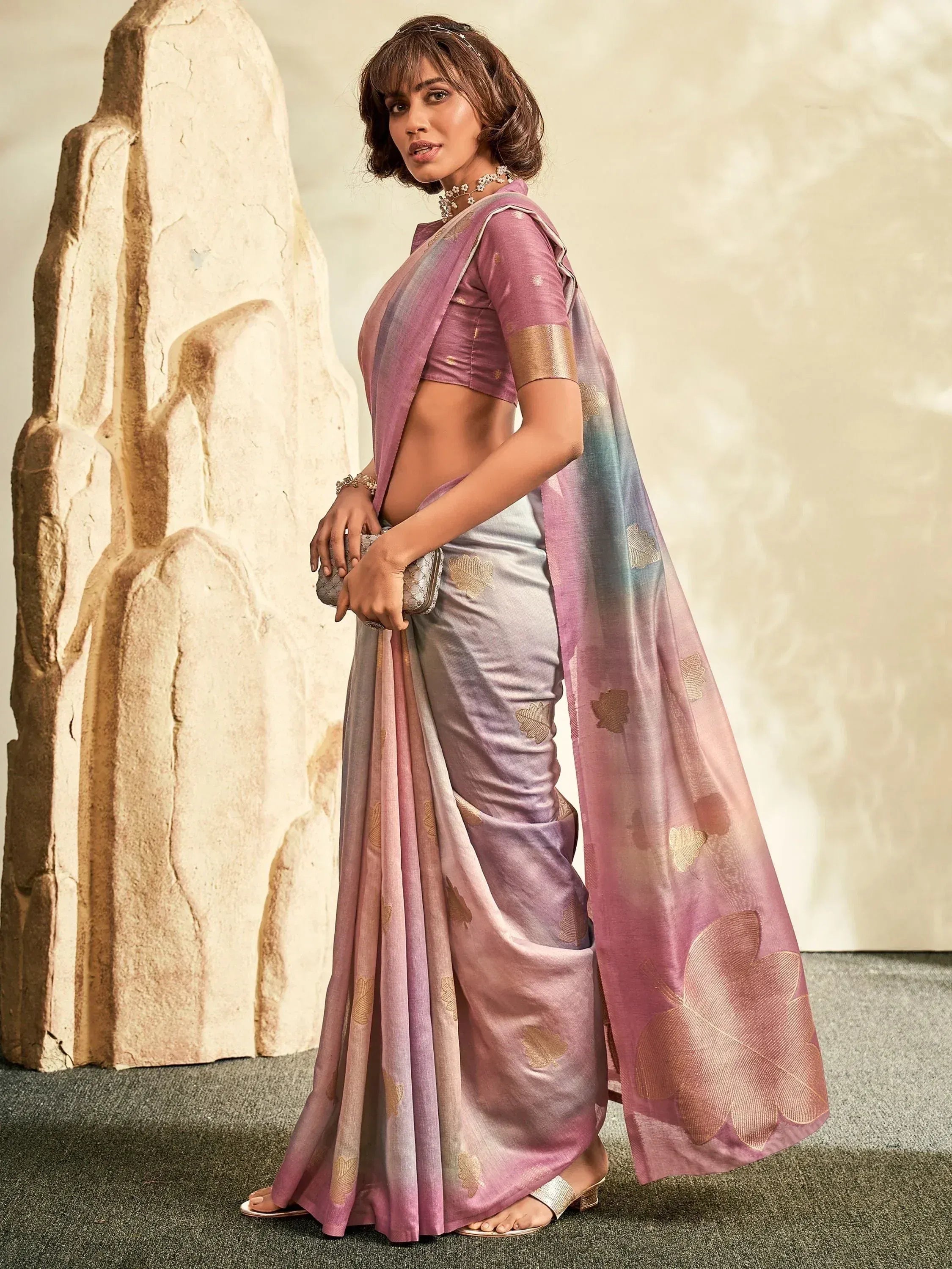 Woman in elegant pastel pink and lavender saree with gold leaf print, styled with matching blouse and jewelry