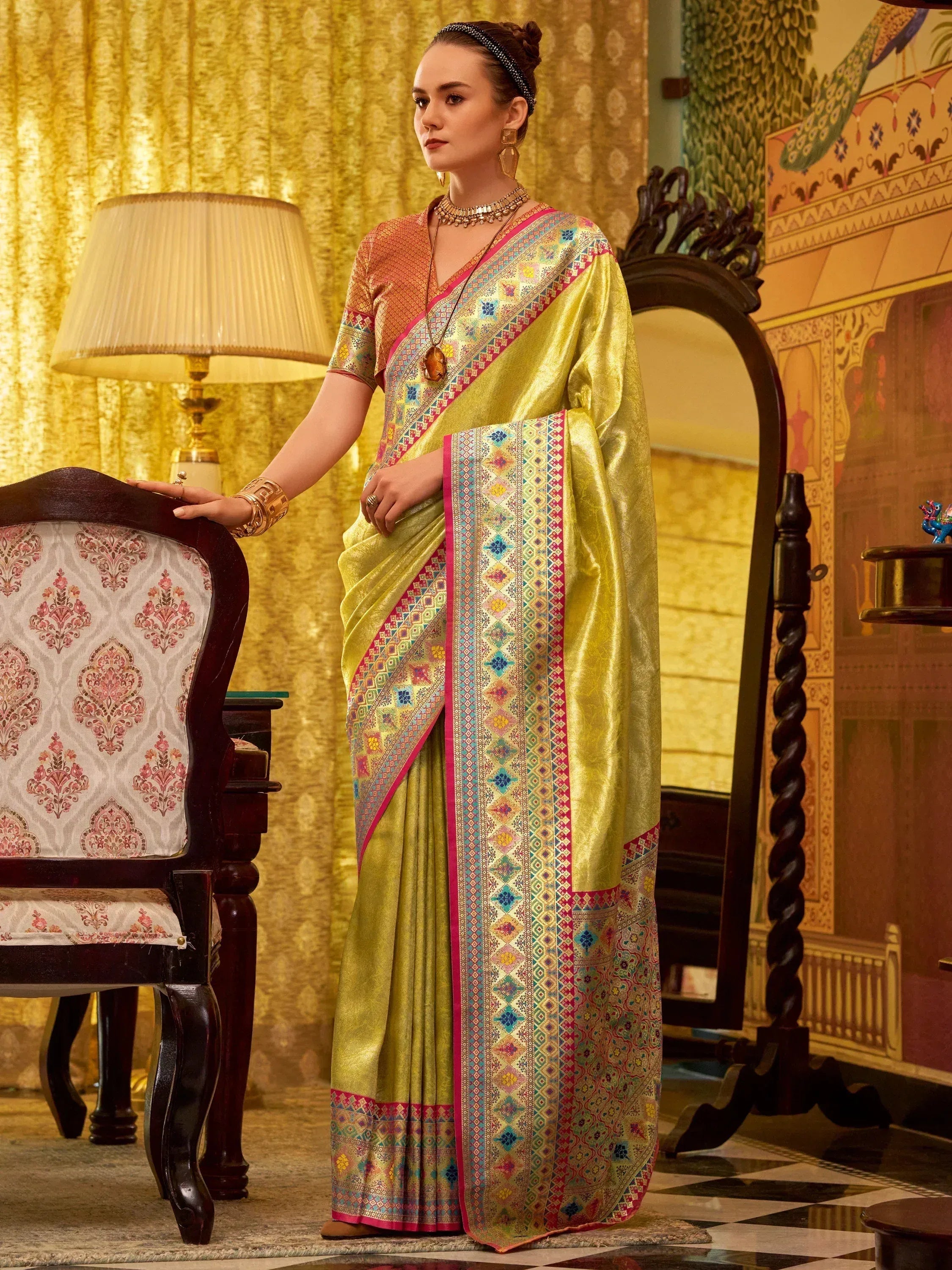 Elegant woman in vibrant yellow saree with colorful geometric border, styled with traditional jewelry and accessories.