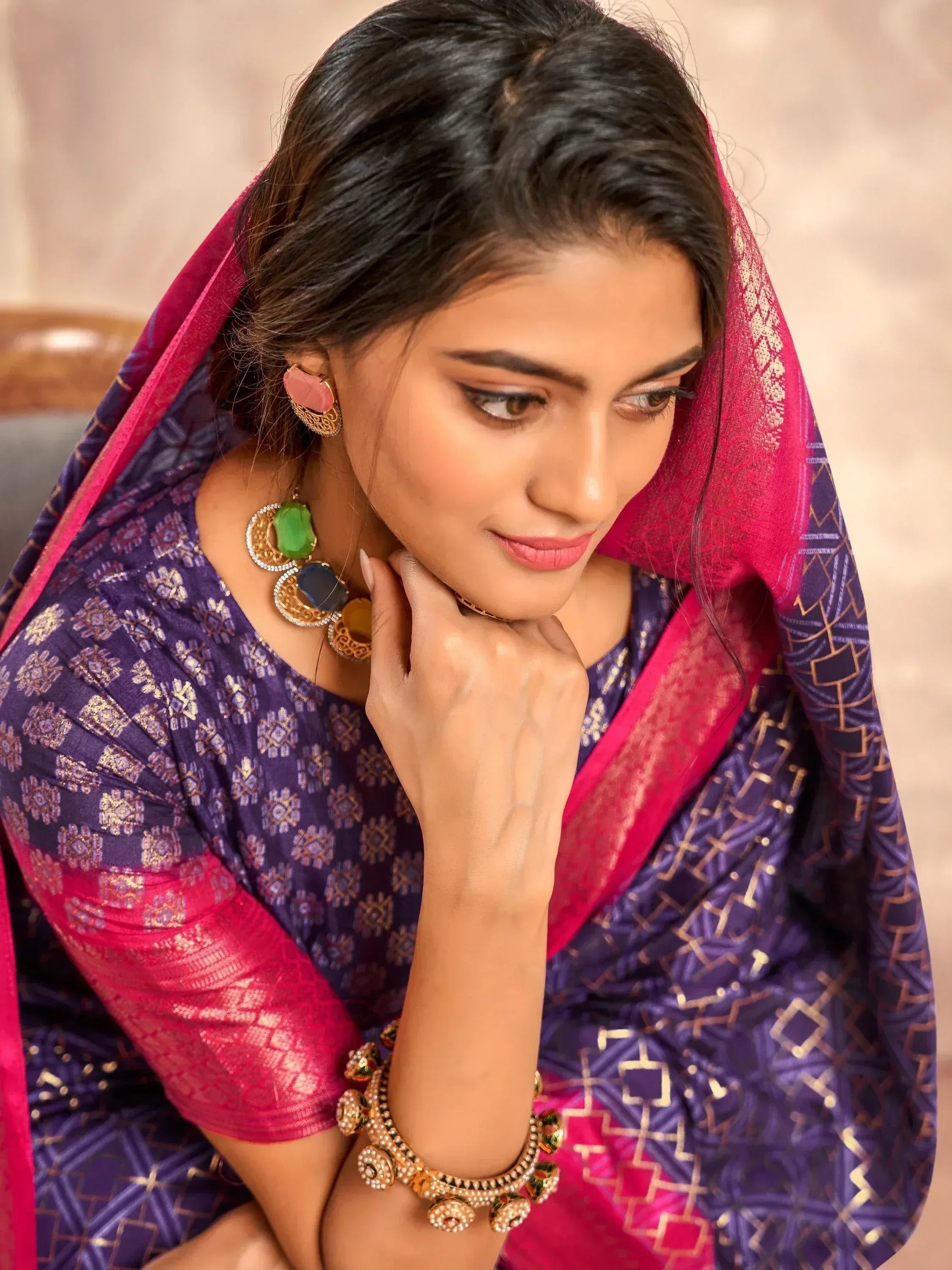 Woman in purple and pink ethnic saree with gold embroidery, statement jewelry, and traditional Indian attire