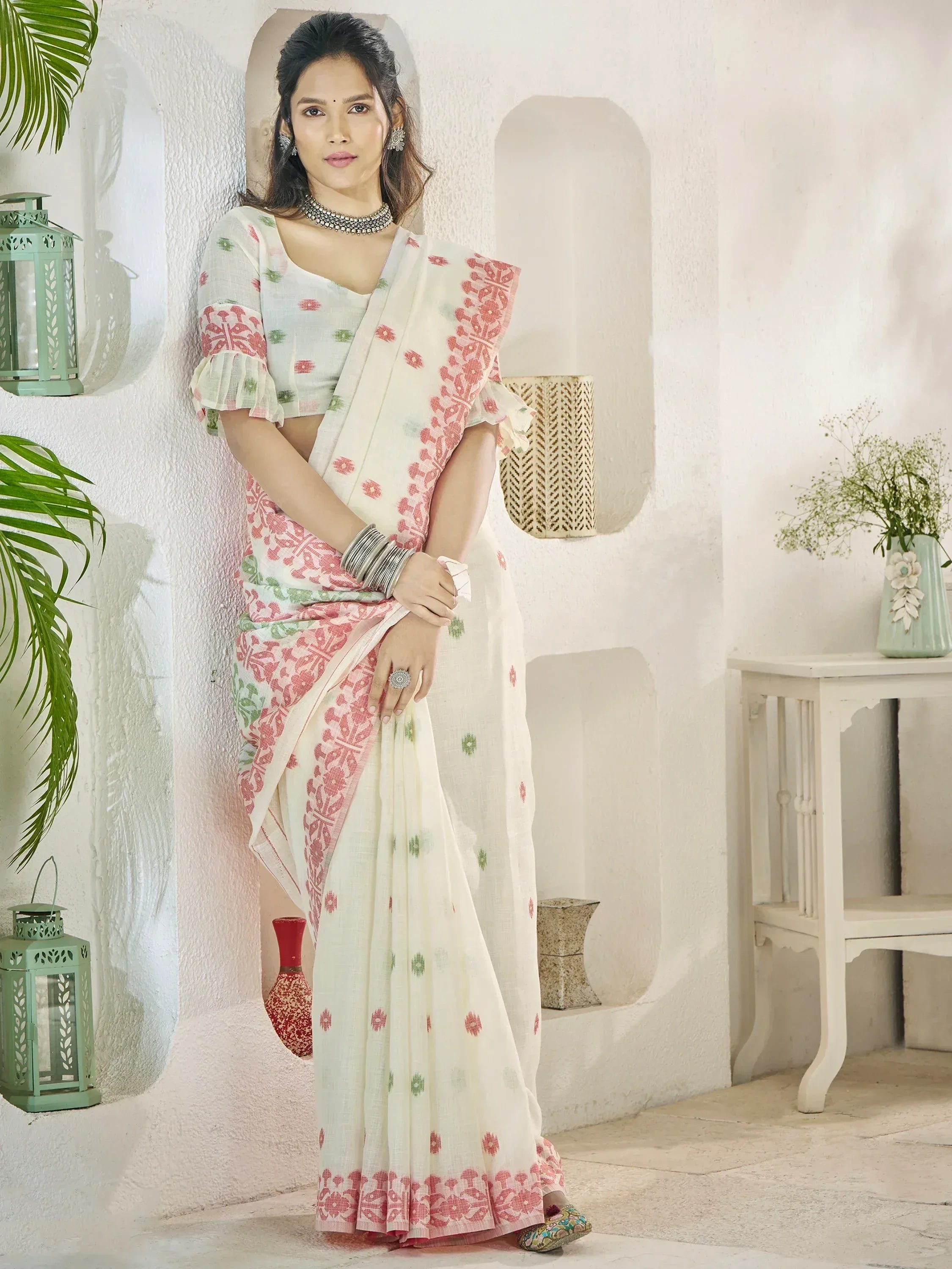 Woman in white saree with pink and green floral print, styled with ruffled blouse and ethnic jewelry