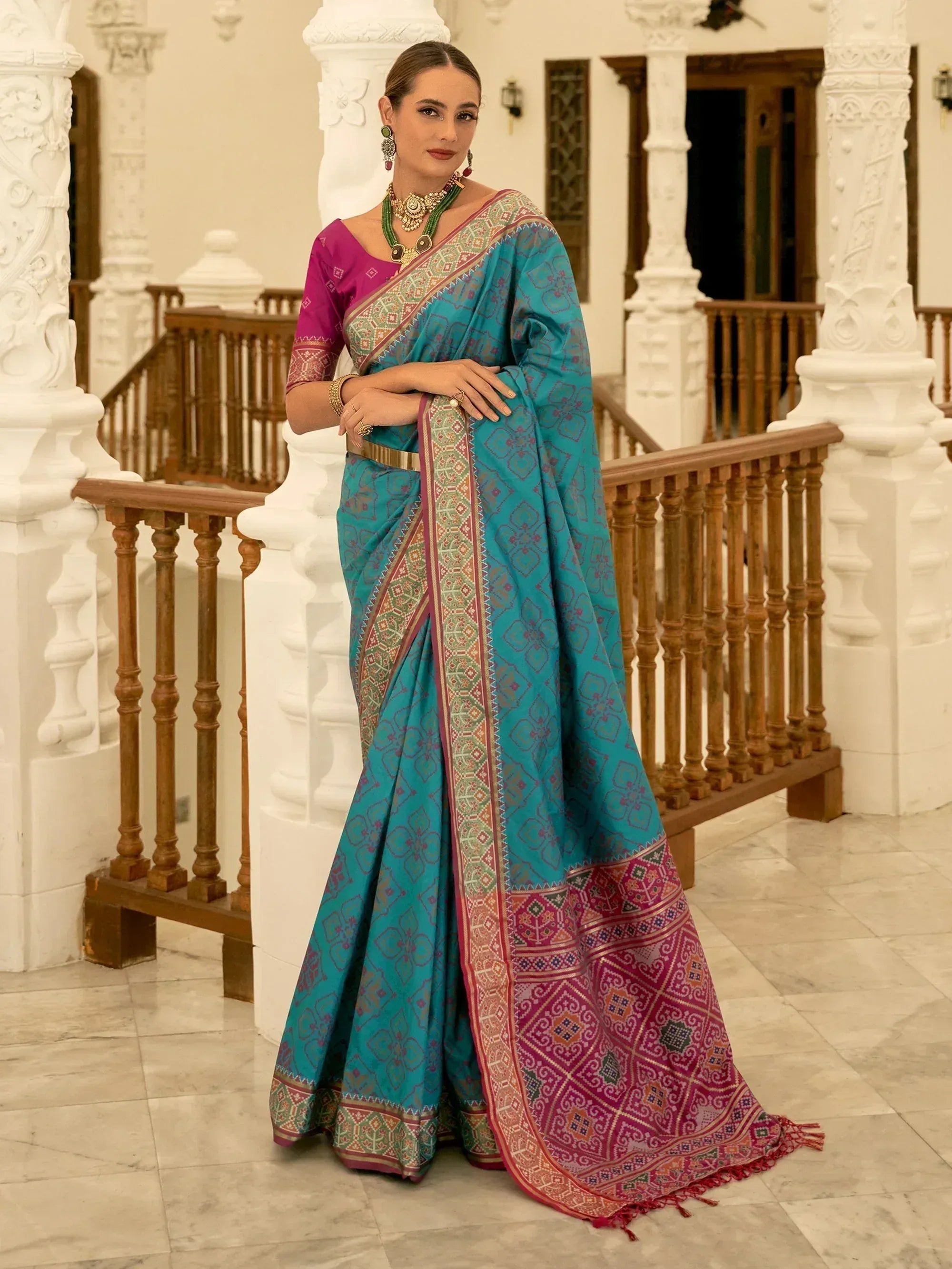 Teal and magenta ethnic saree with intricate geometric patterns, paired with matching blouse and traditional jewelry.