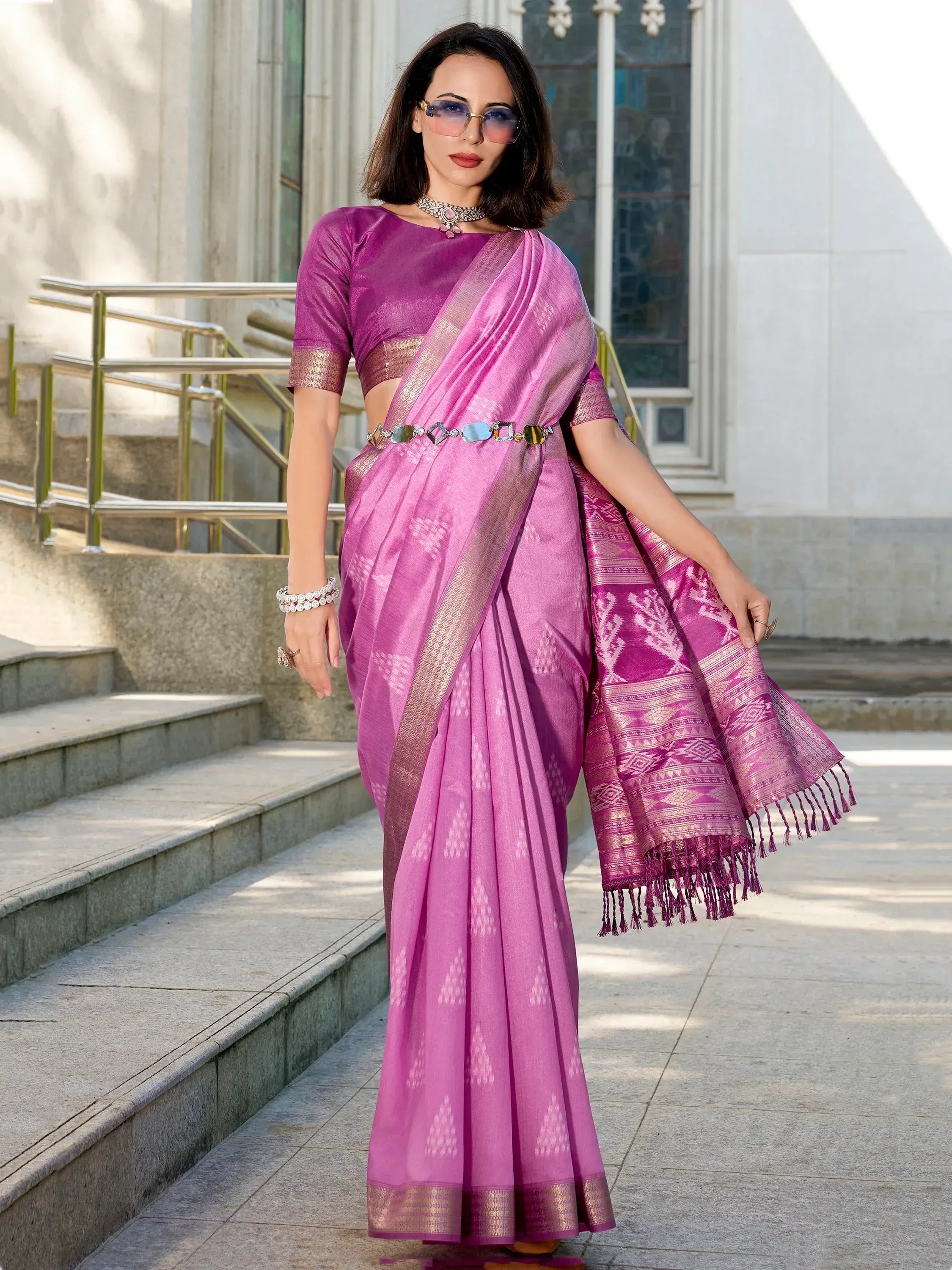 Purple designer saree with gold border and tassels, styled with statement jewelry and sunglasses