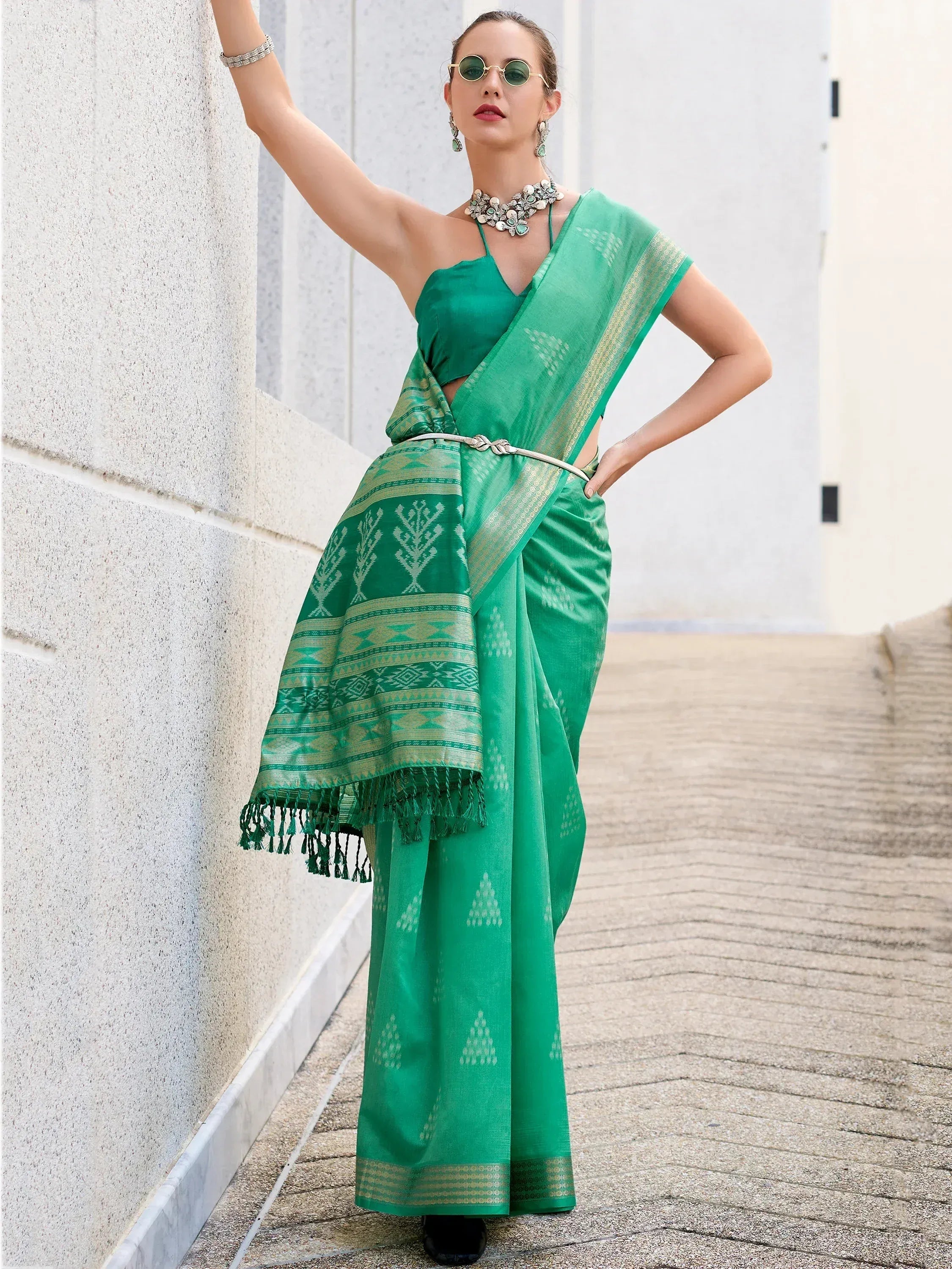 Green ethnic saree with gold border and geometric patterns, paired with statement jewelry and sunglasses