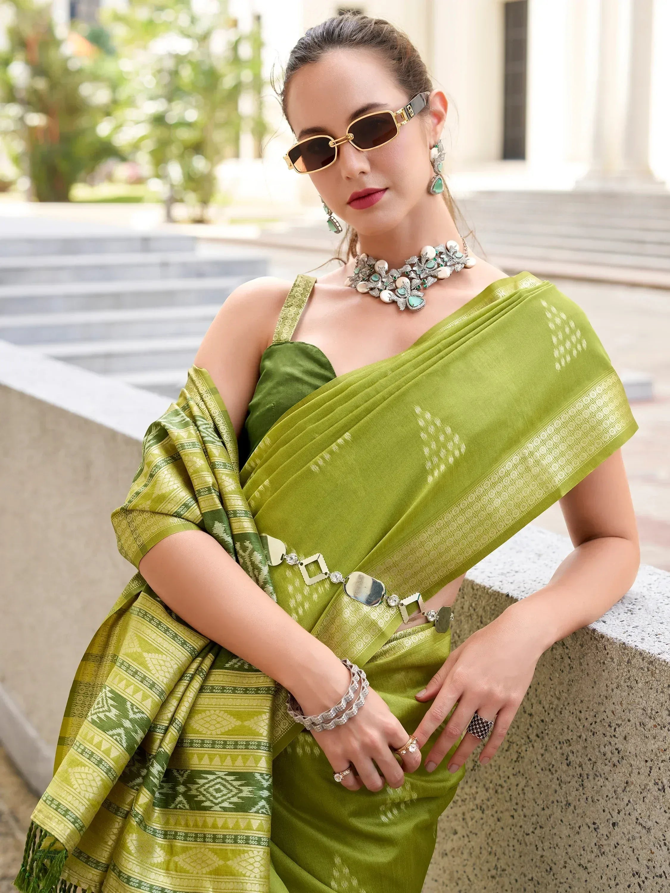 Elegant green saree with geometric patterns, styled with statement jewelry and sunglasses for a modern ethnic look.