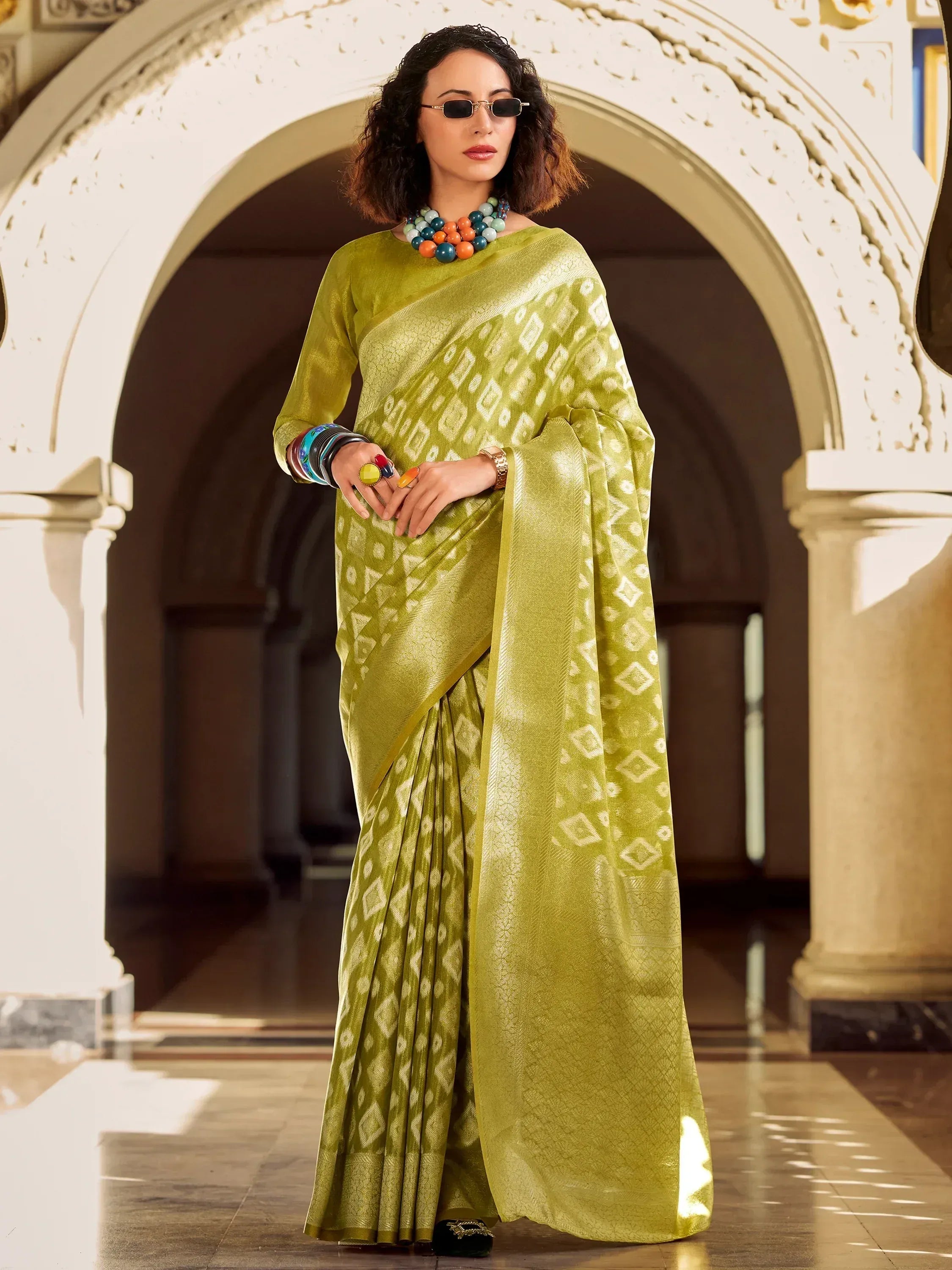 Elegant green saree with geometric patterns, styled with colorful jewelry and sunglasses