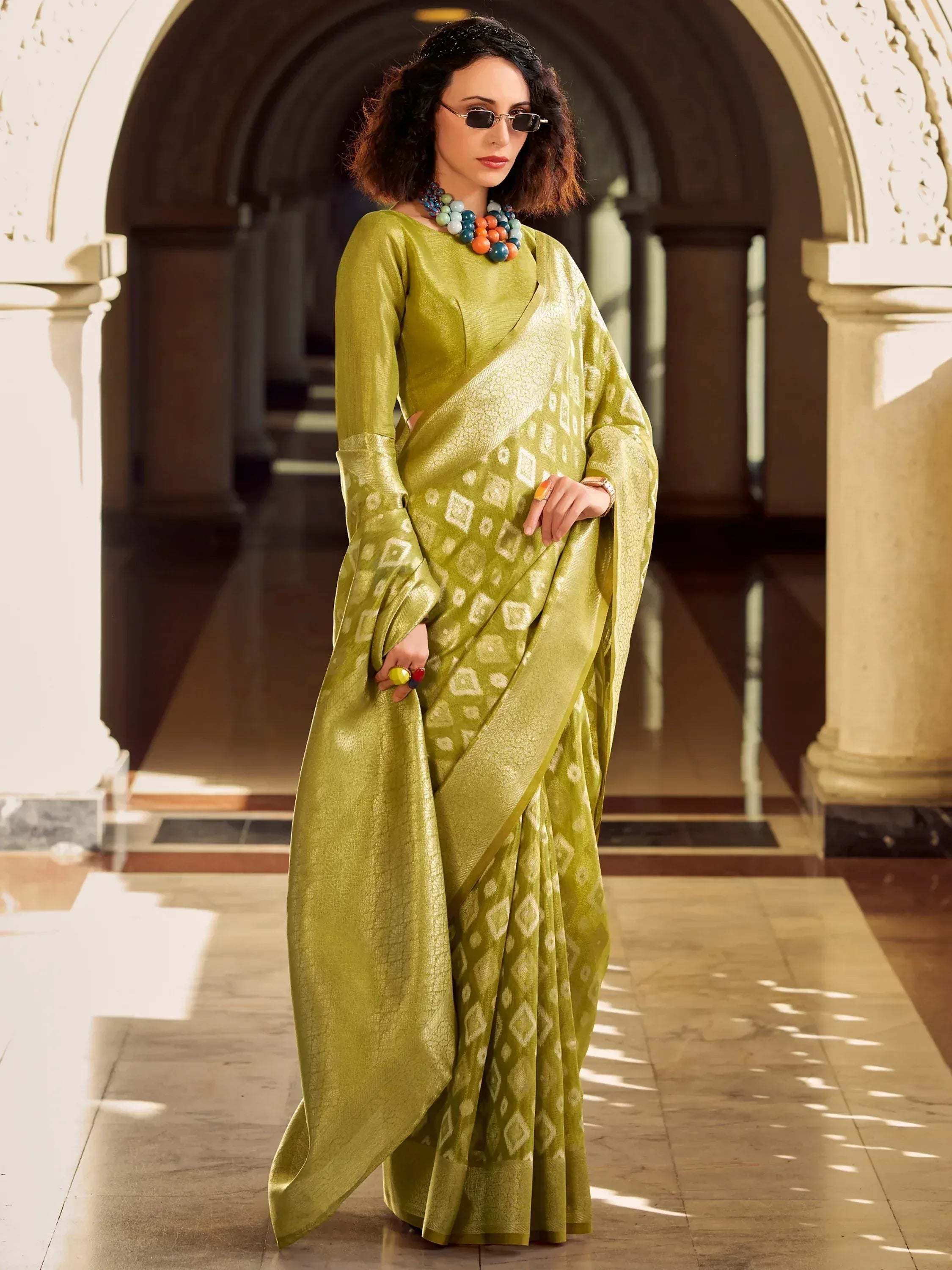 Elegant green saree with geometric patterns, styled with colorful jewelry and sunglasses.