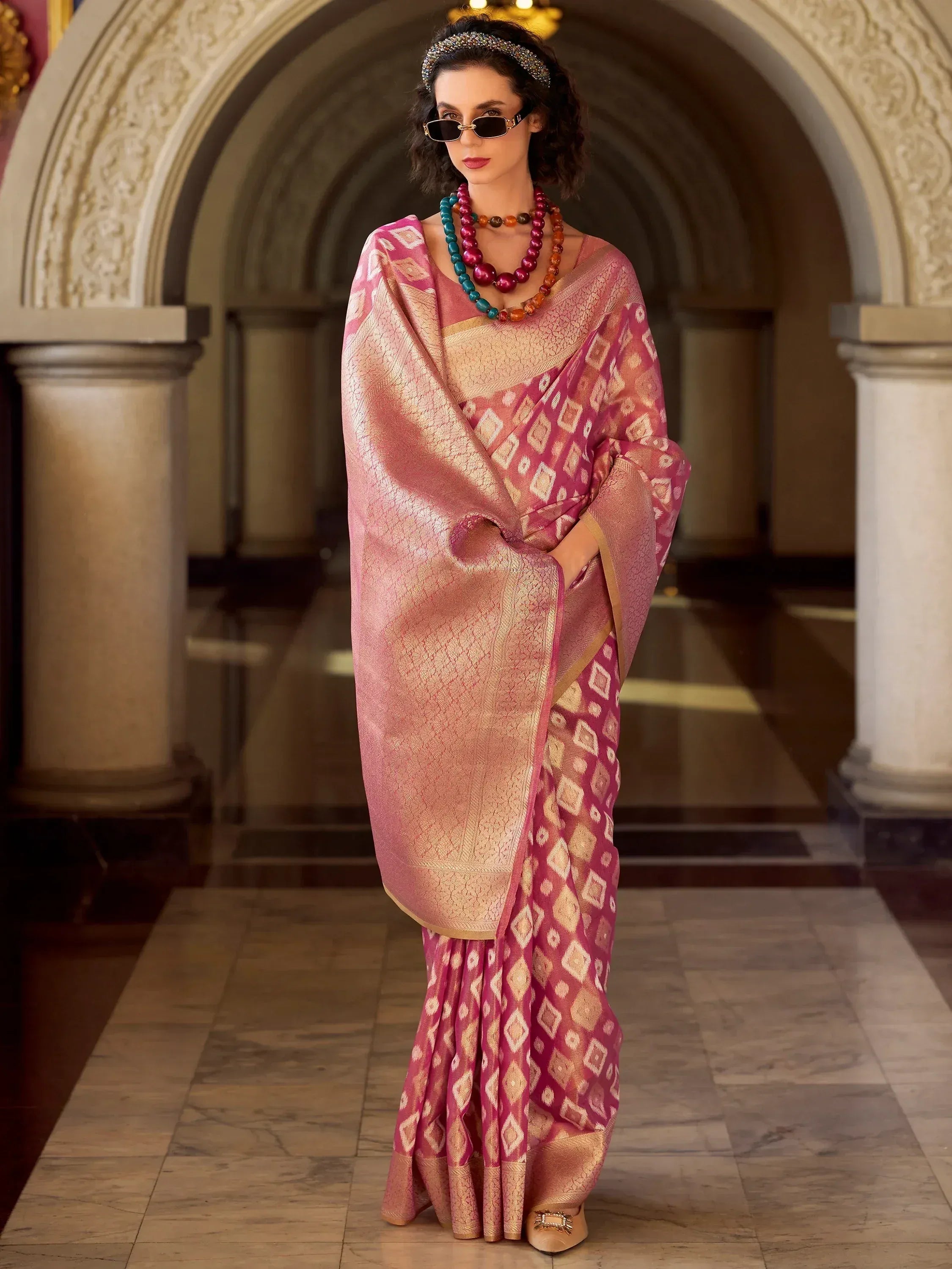 Elegant pink and gold ethnic saree with geometric patterns, styled with statement jewelry and sunglasses.