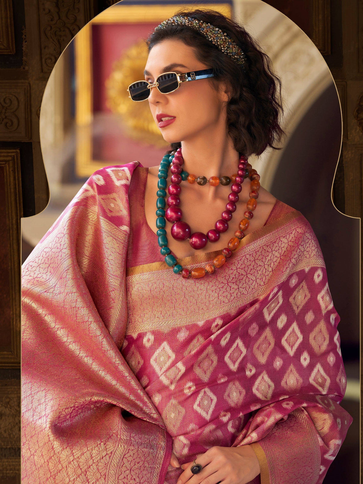 Woman in pink ethnic saree with gold patterns, layered beaded necklaces, and sunglasses, styled for Indian fashion.
