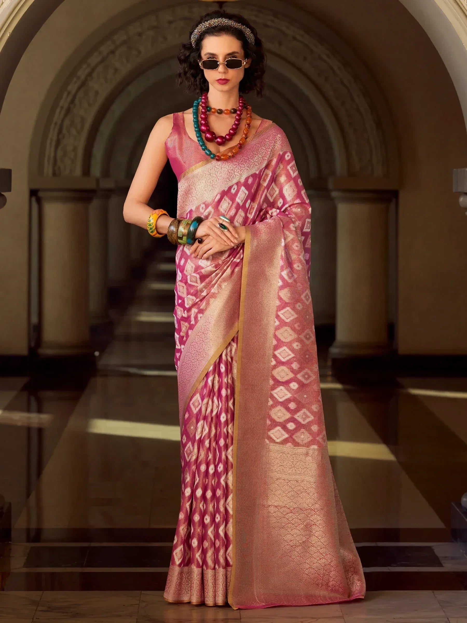 Elegant pink saree with geometric patterns, paired with colorful jewelry and sunglasses for a stylish ethnic look.