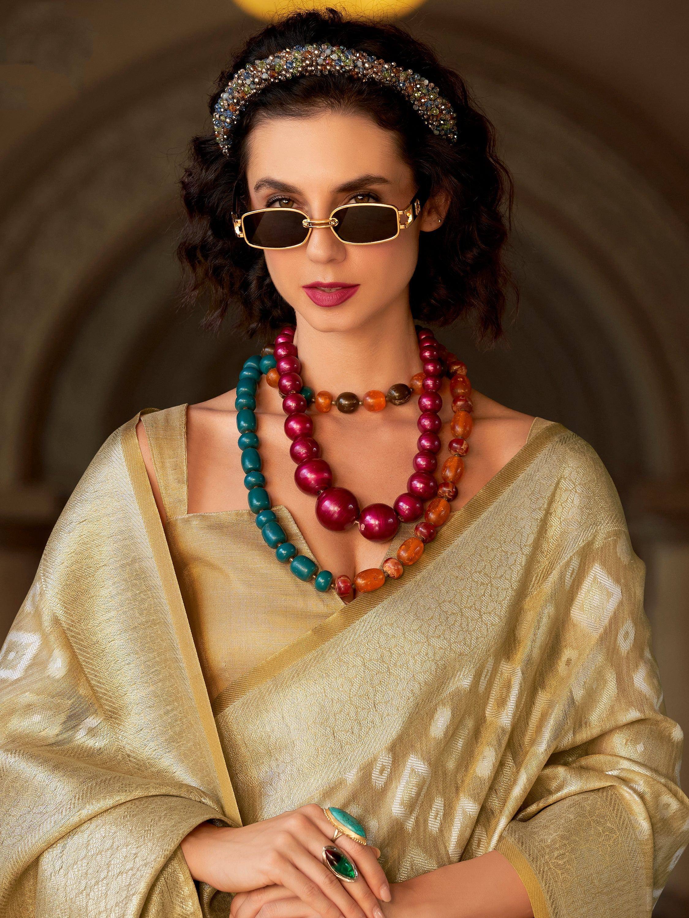 Woman in golden ethnic saree with colorful beaded necklaces, jeweled headband, and sunglasses