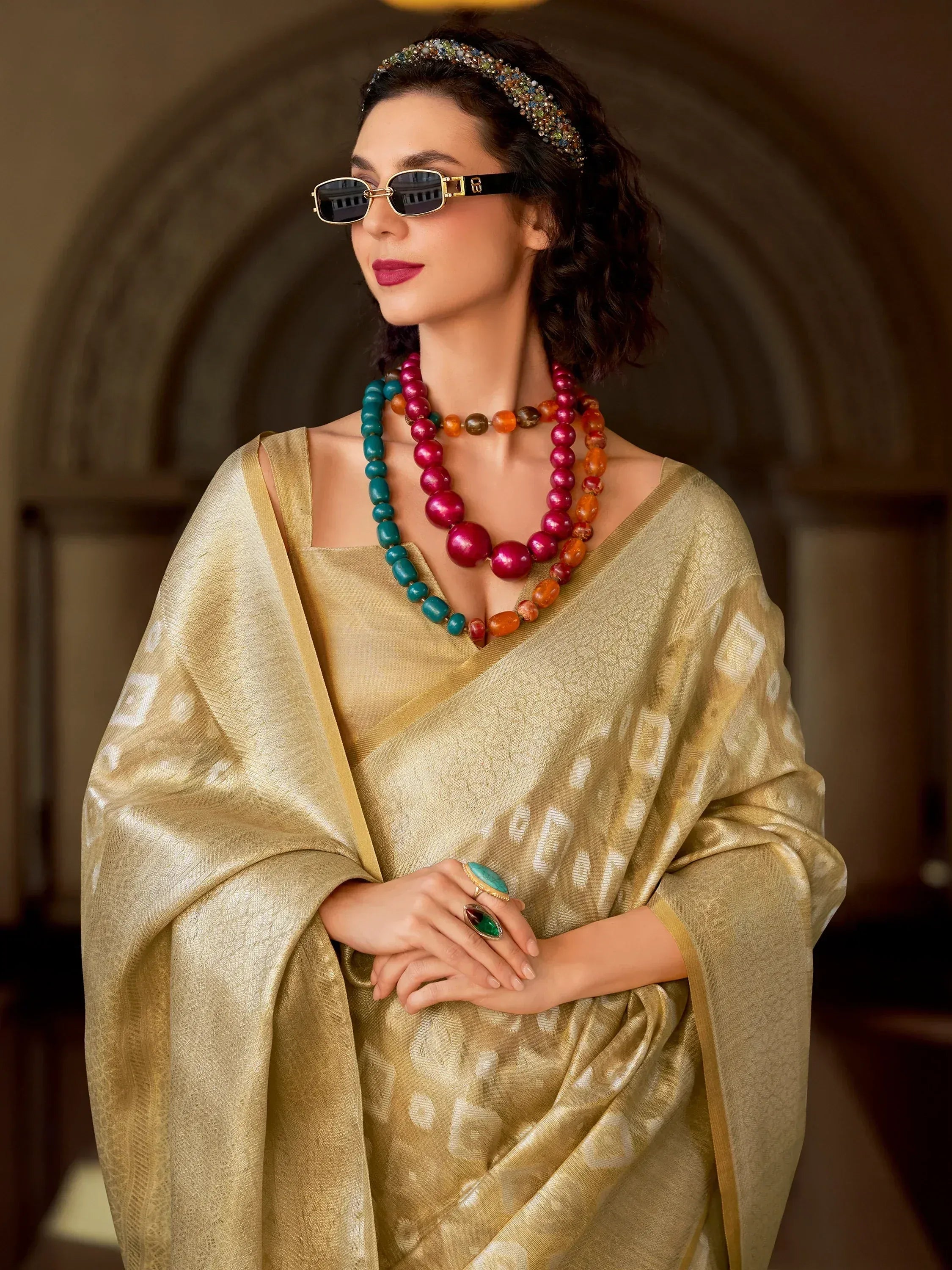 Woman in golden ethnic saree with colorful bead necklaces and sunglasses, styled for festive occasions.