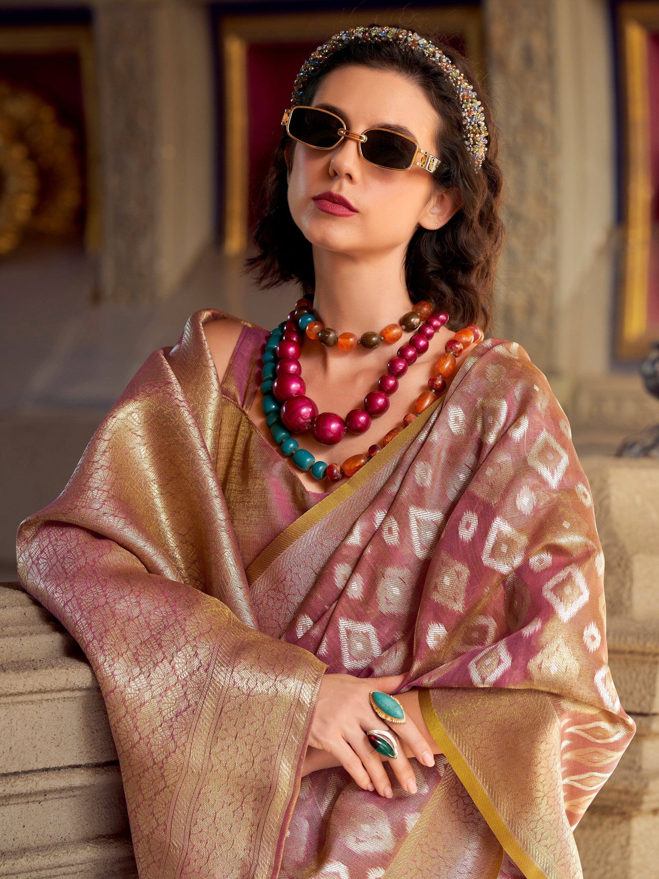 Woman in elegant pink and gold saree with statement jewelry and sunglasses, showcasing ethnic fashion.