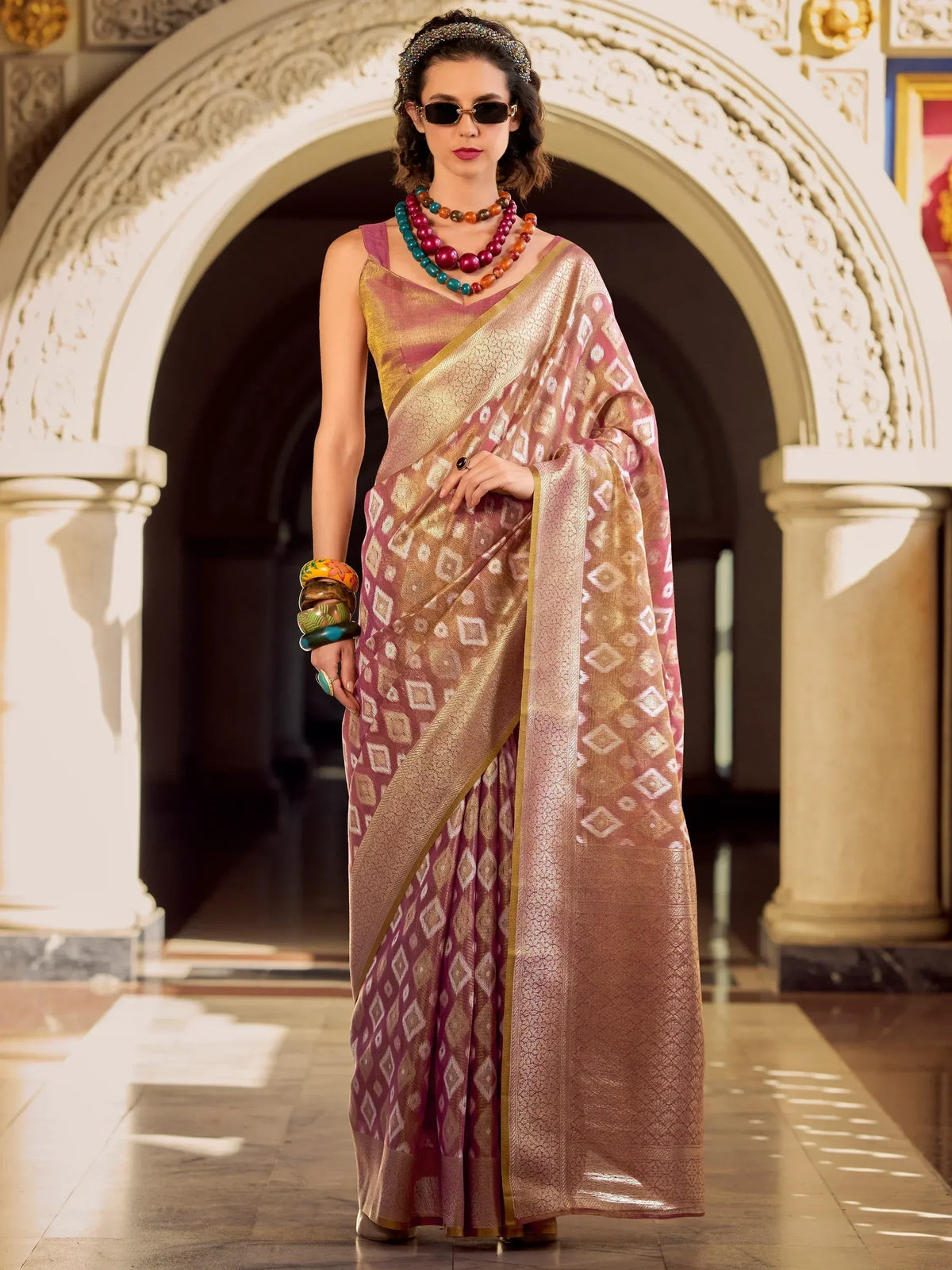 Woman in elegant pink and gold ethnic saree with geometric print, styled with statement jewelry and sunglasses