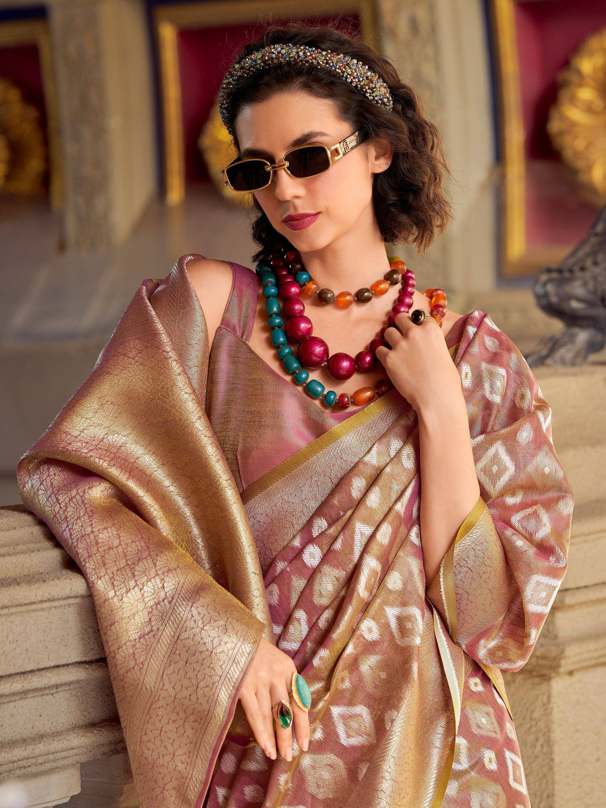 Woman in elegant pink and gold saree with statement jewelry and sunglasses, showcasing Indian ethnic wear.