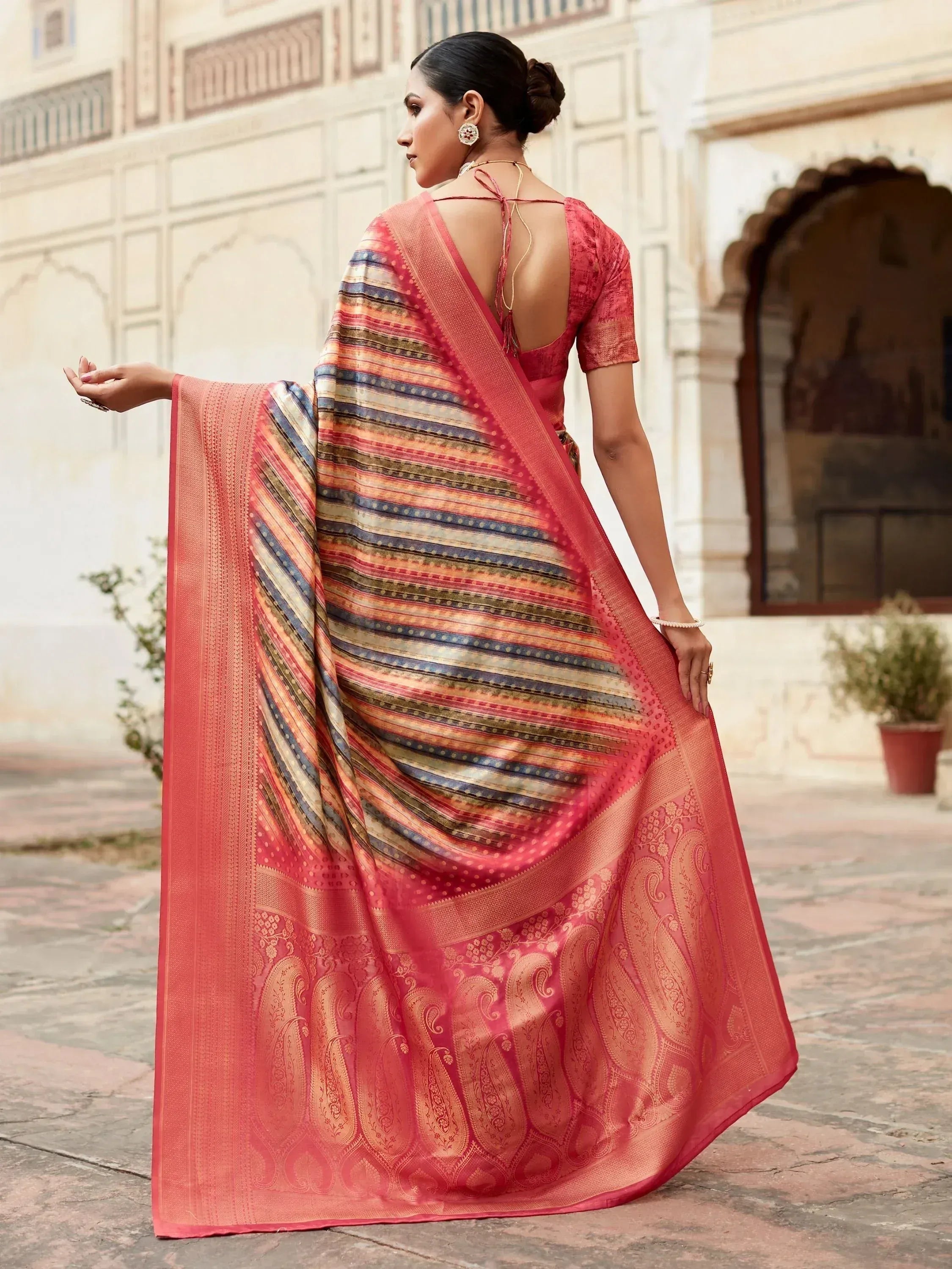 Woman in coral pink designer saree with striped and paisley motifs, backless blouse, traditional Indian ethnic wear