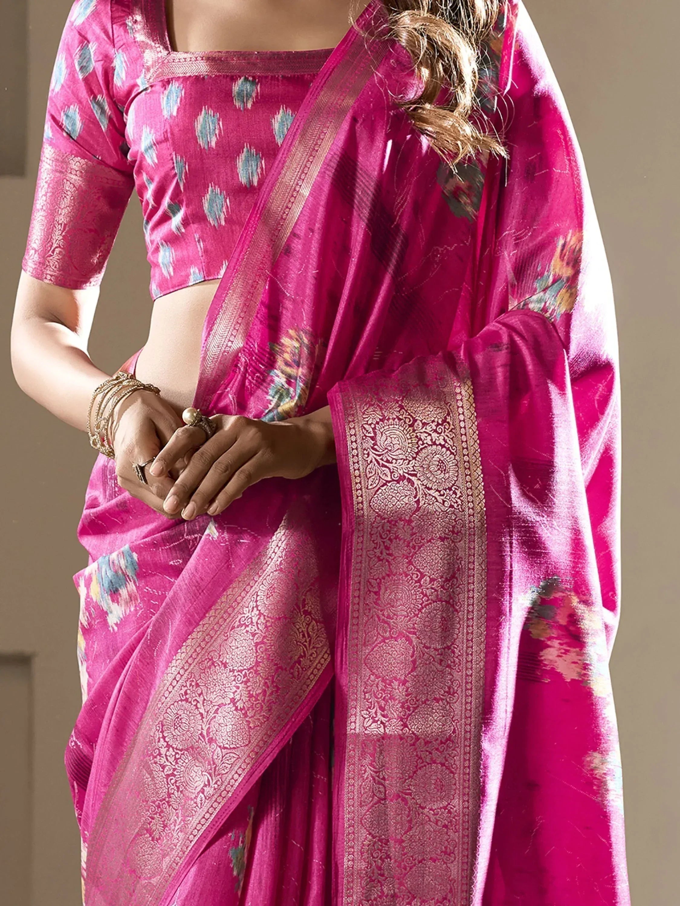 Vibrant pink designer saree with floral ikat print and gold zari border, paired with matching blouse for ethnic wear