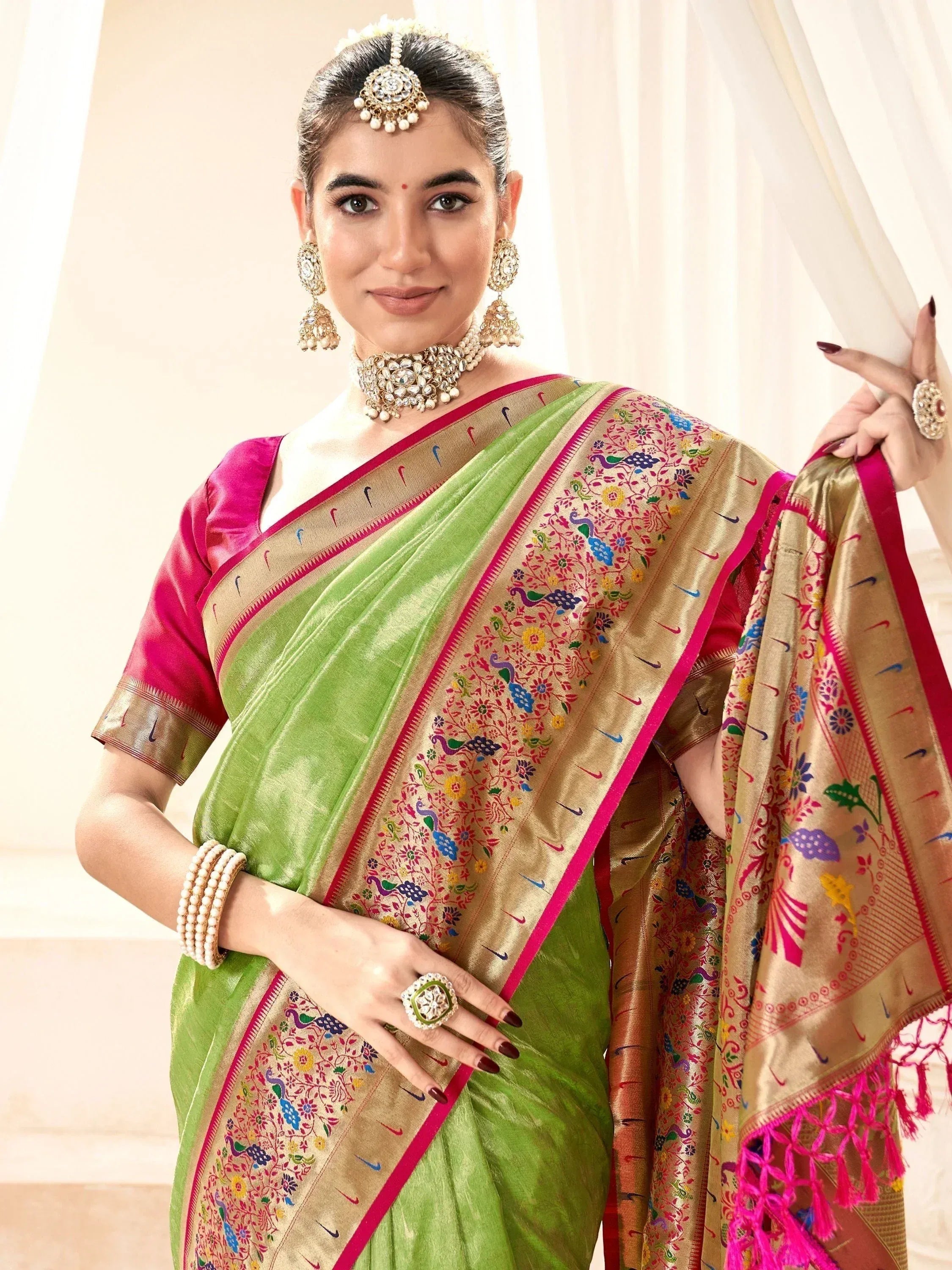 Green and gold embroidered saree with peacock motifs, paired with pink blouse and traditional jewelry