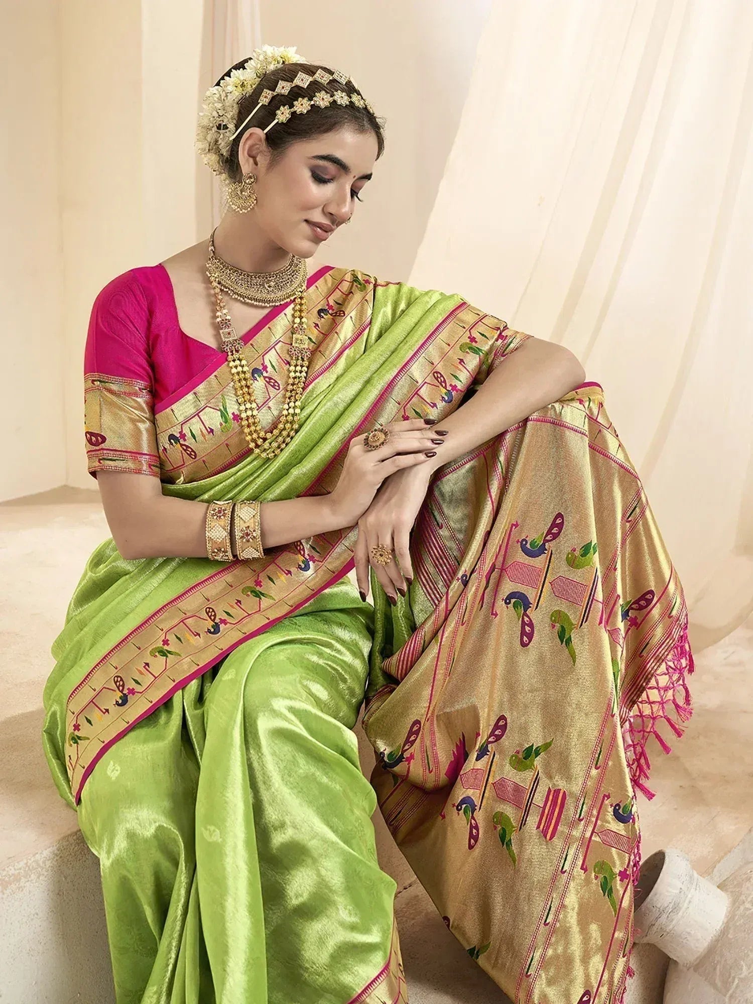 Woman in vibrant green and gold Indian saree with peacock print, paired with pink blouse and traditional jewelry