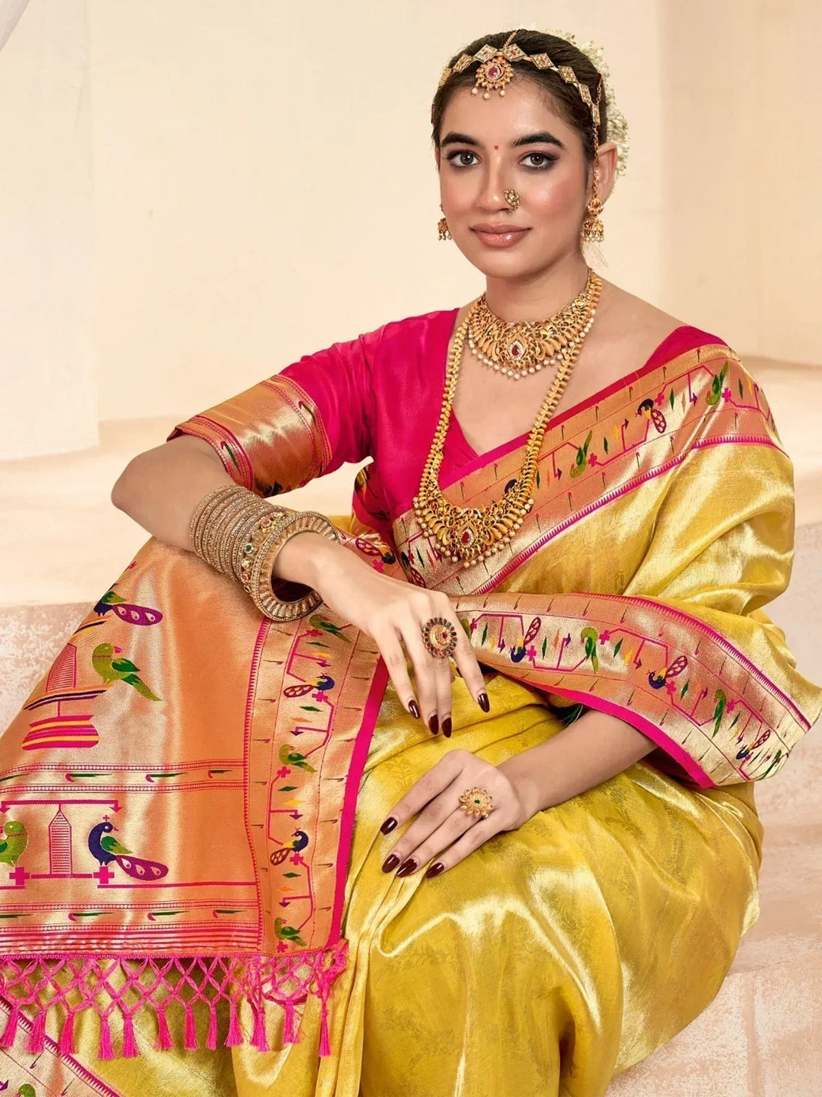 Woman in vibrant yellow and pink embroidered saree with peacock motifs, traditional gold jewelry, and festive ethnic wear