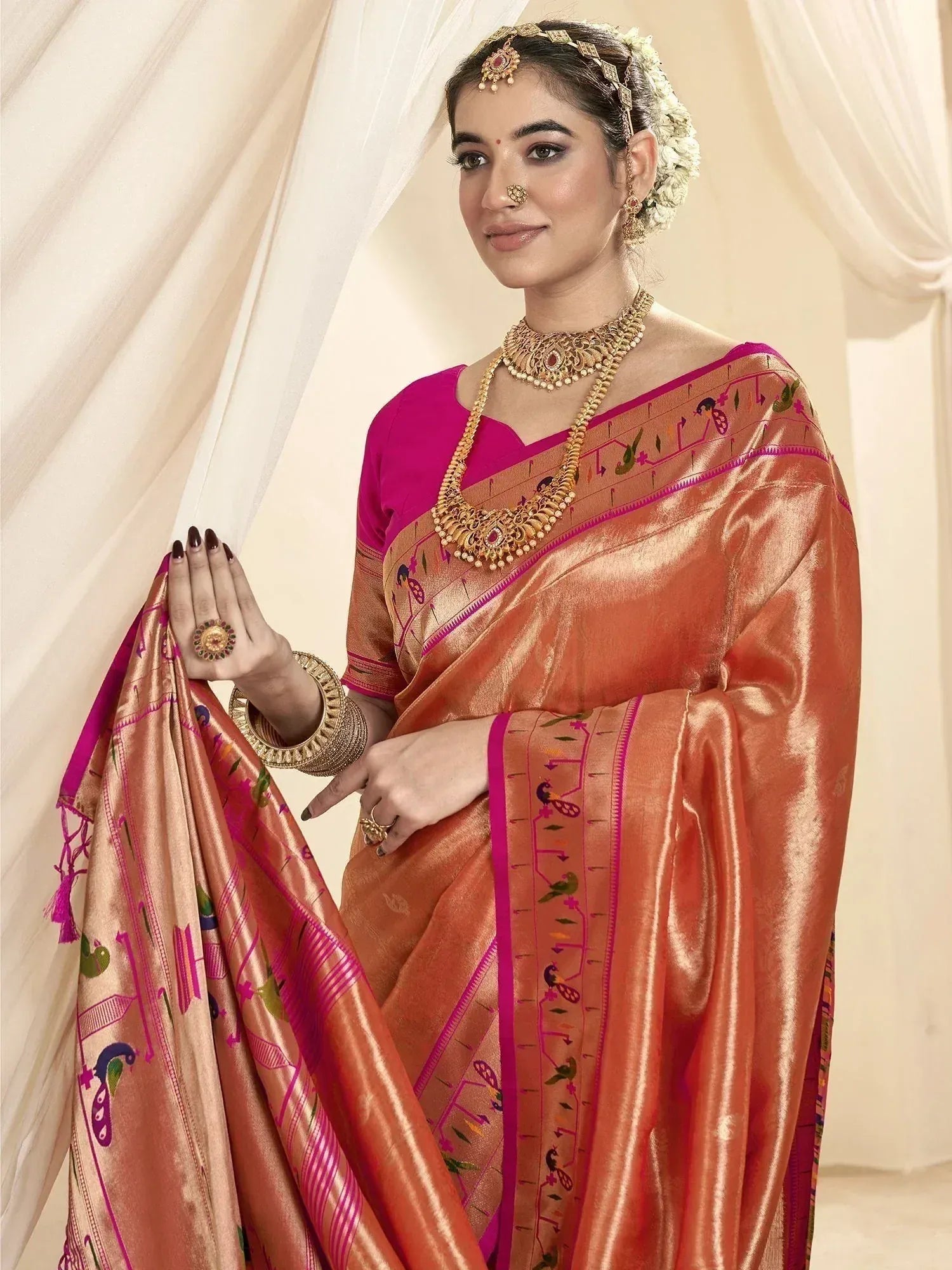 Woman in traditional Indian saree with peacock embroidery, gold jewelry, and floral hair accessory