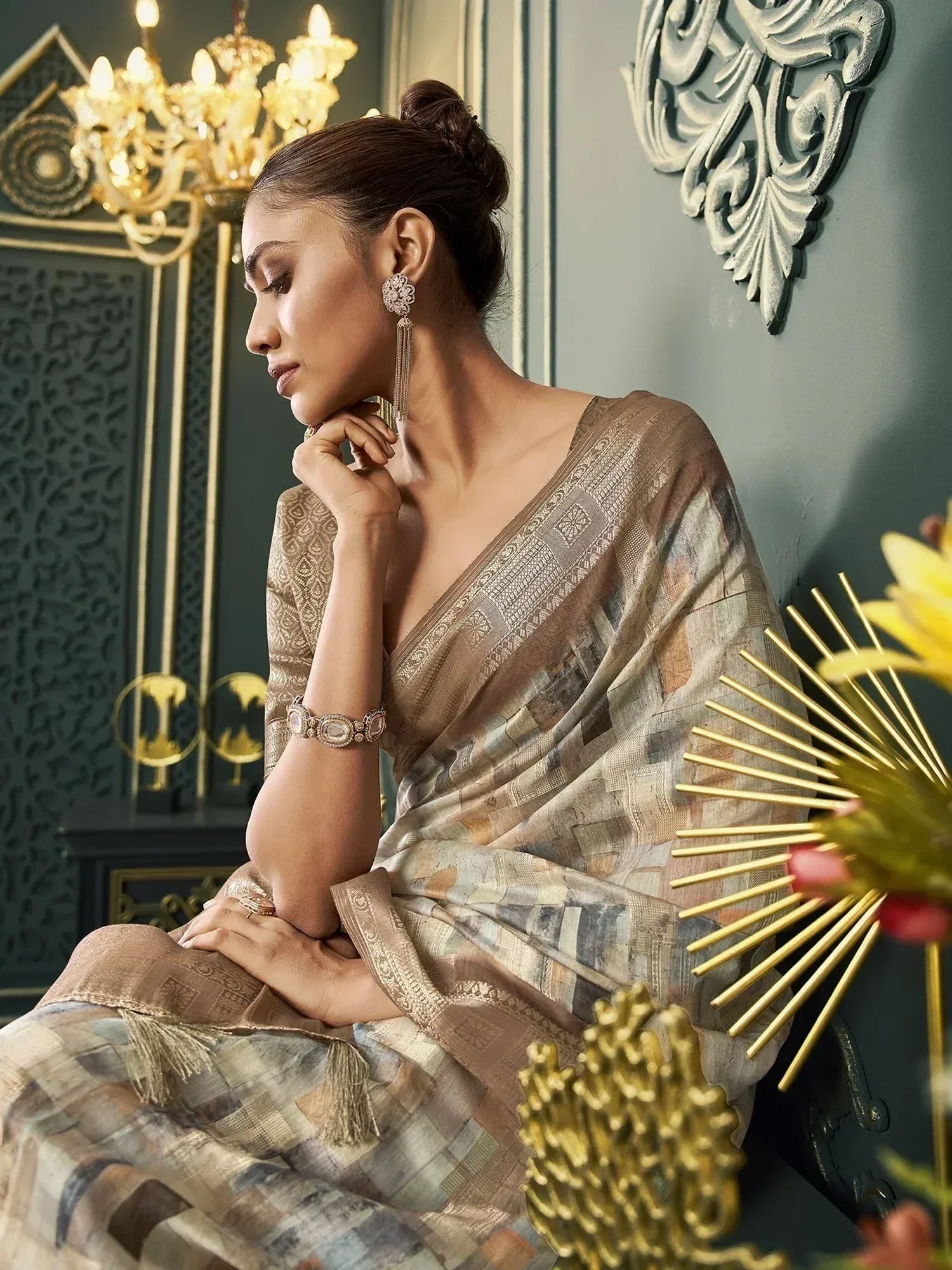 Elegant woman in designer saree with intricate patterns, gold jewelry, and chandelier backdrop