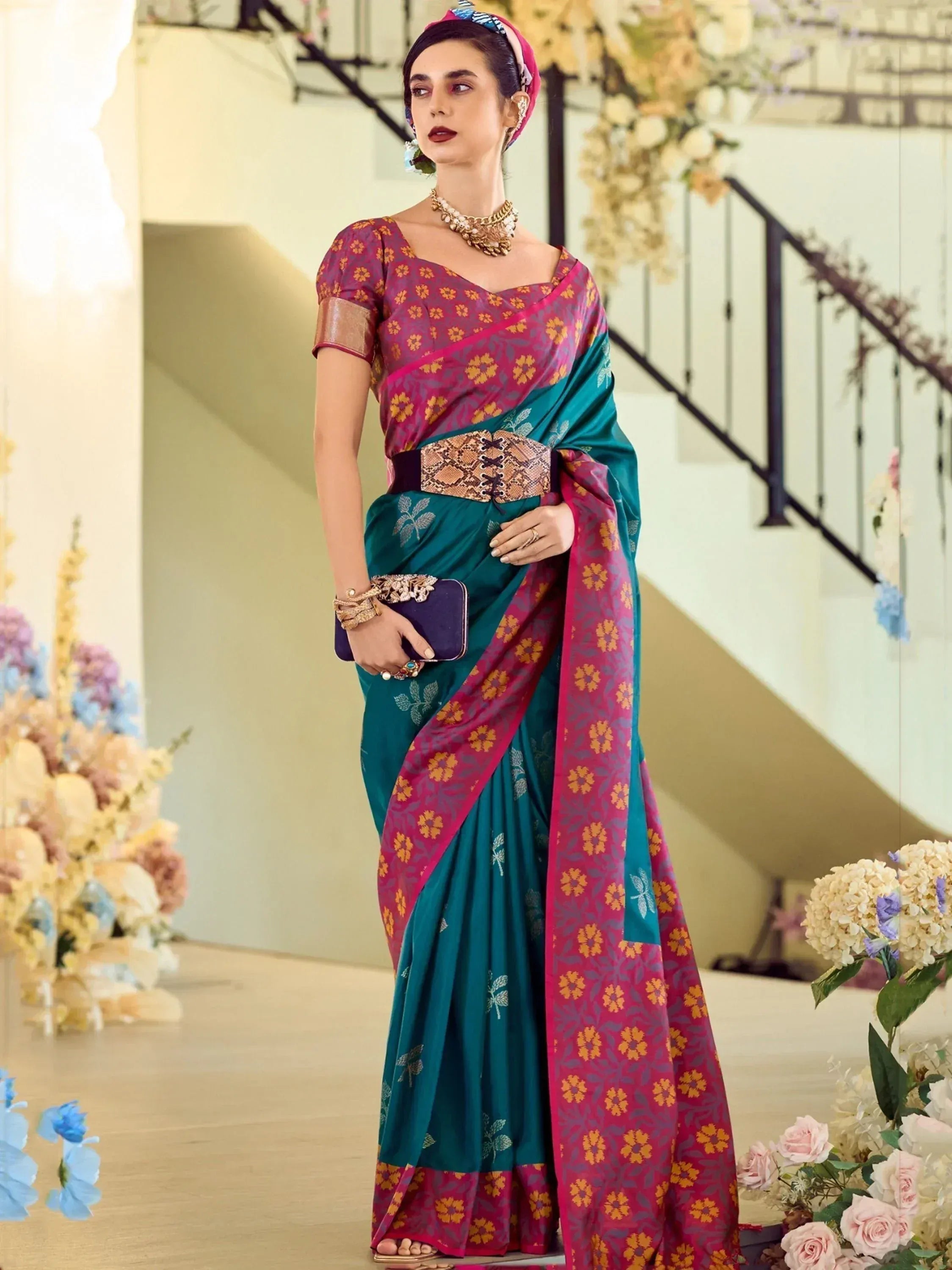 Woman in vibrant teal and magenta floral saree with gold blouse, styled for festive occasions