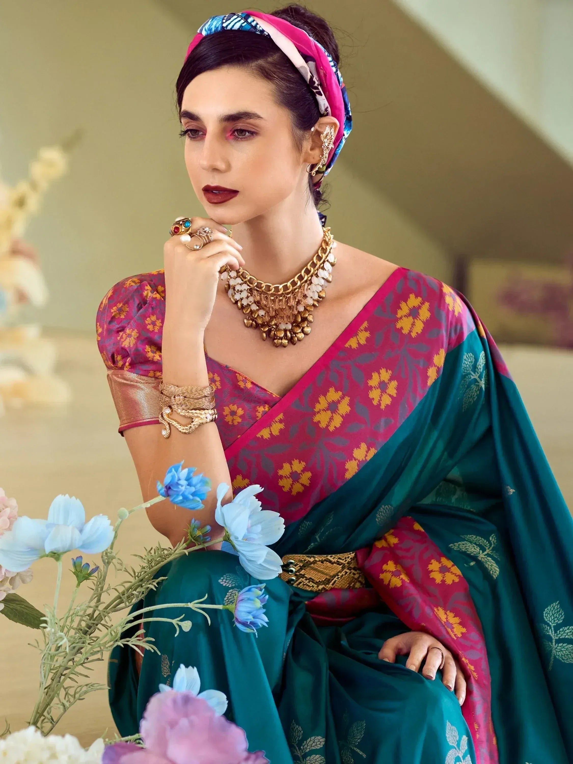 Woman in vibrant ethnic saree with floral print, gold jewelry, and colorful headscarf, styled for festive occasions.