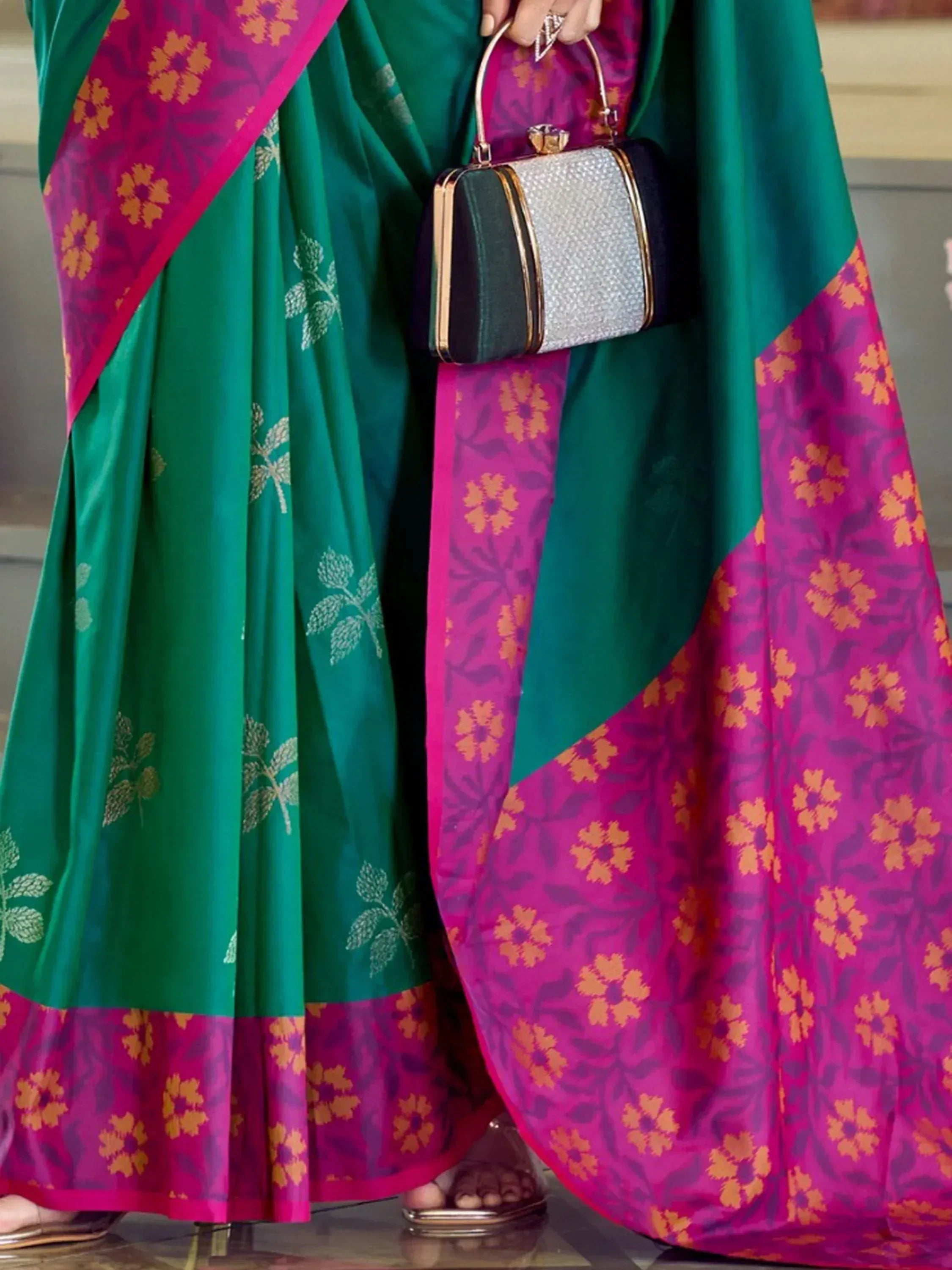 Green and magenta floral saree with gold leaf print, paired with a silver clutch for Indian ethnic wear.