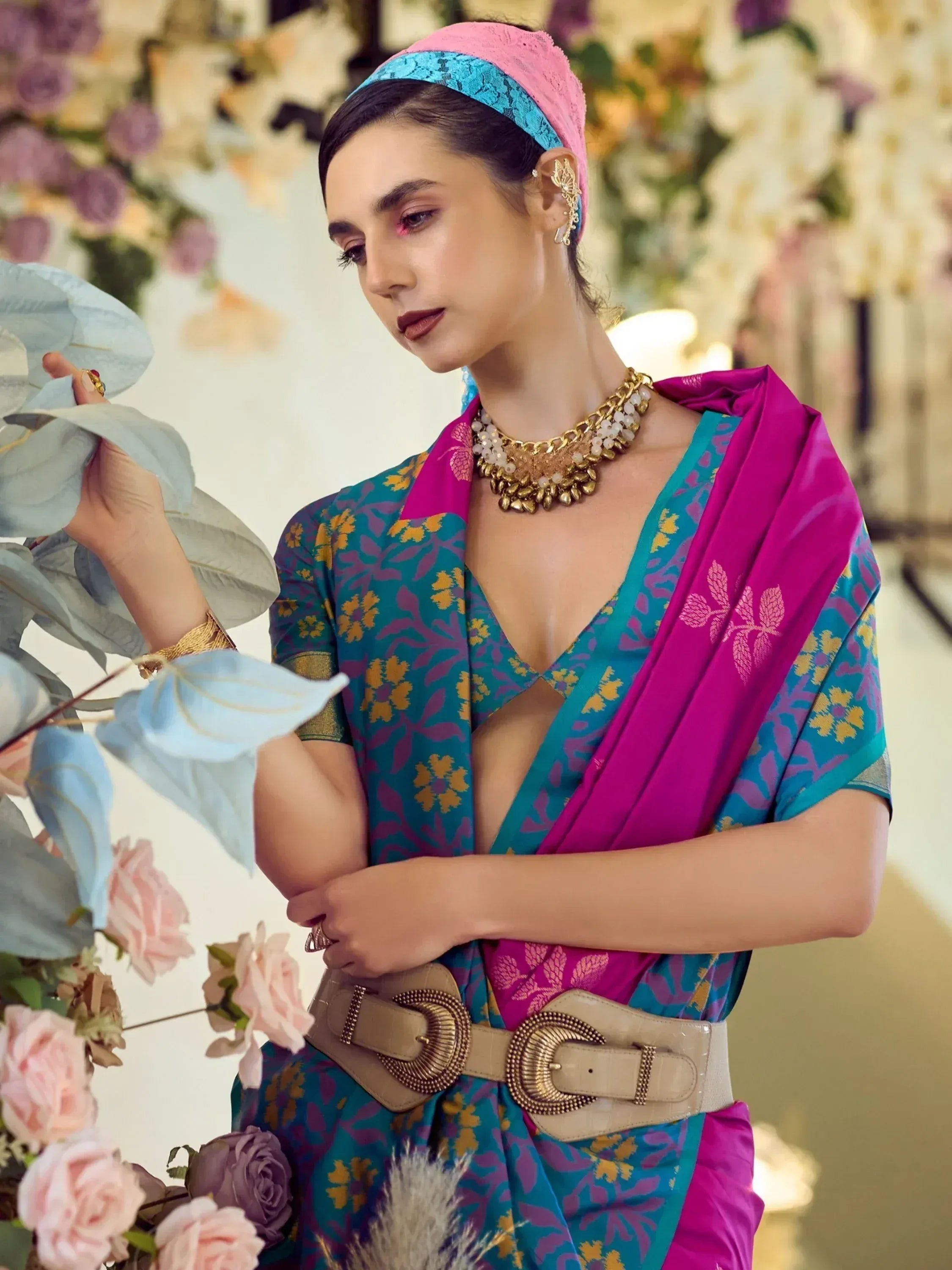 Woman in vibrant teal and magenta floral saree with gold jewelry and lace headband, styled for ethnic occasions