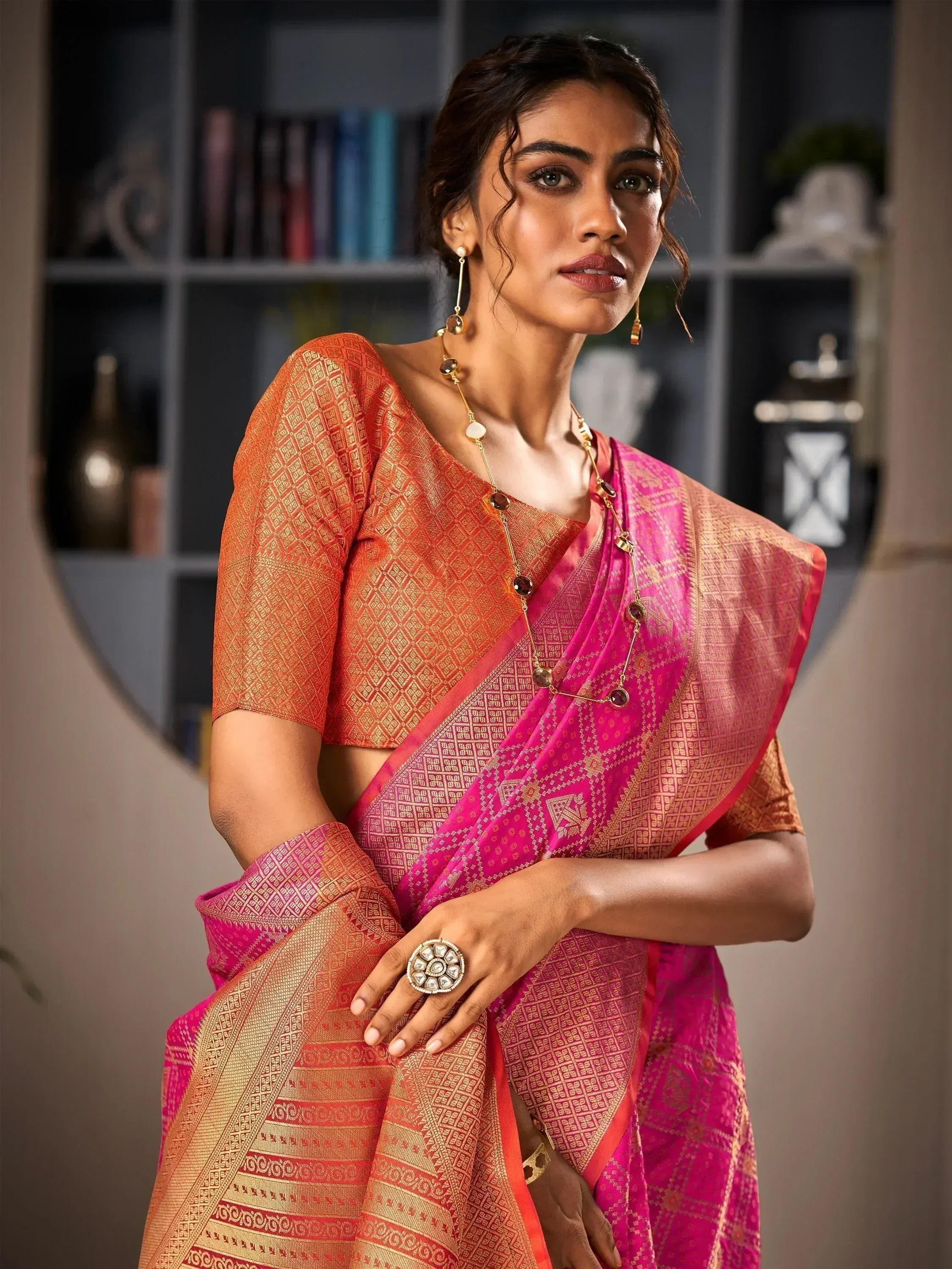 Woman in vibrant pink and orange ethnic saree with gold patterns, styled with traditional jewelry for festive occasions