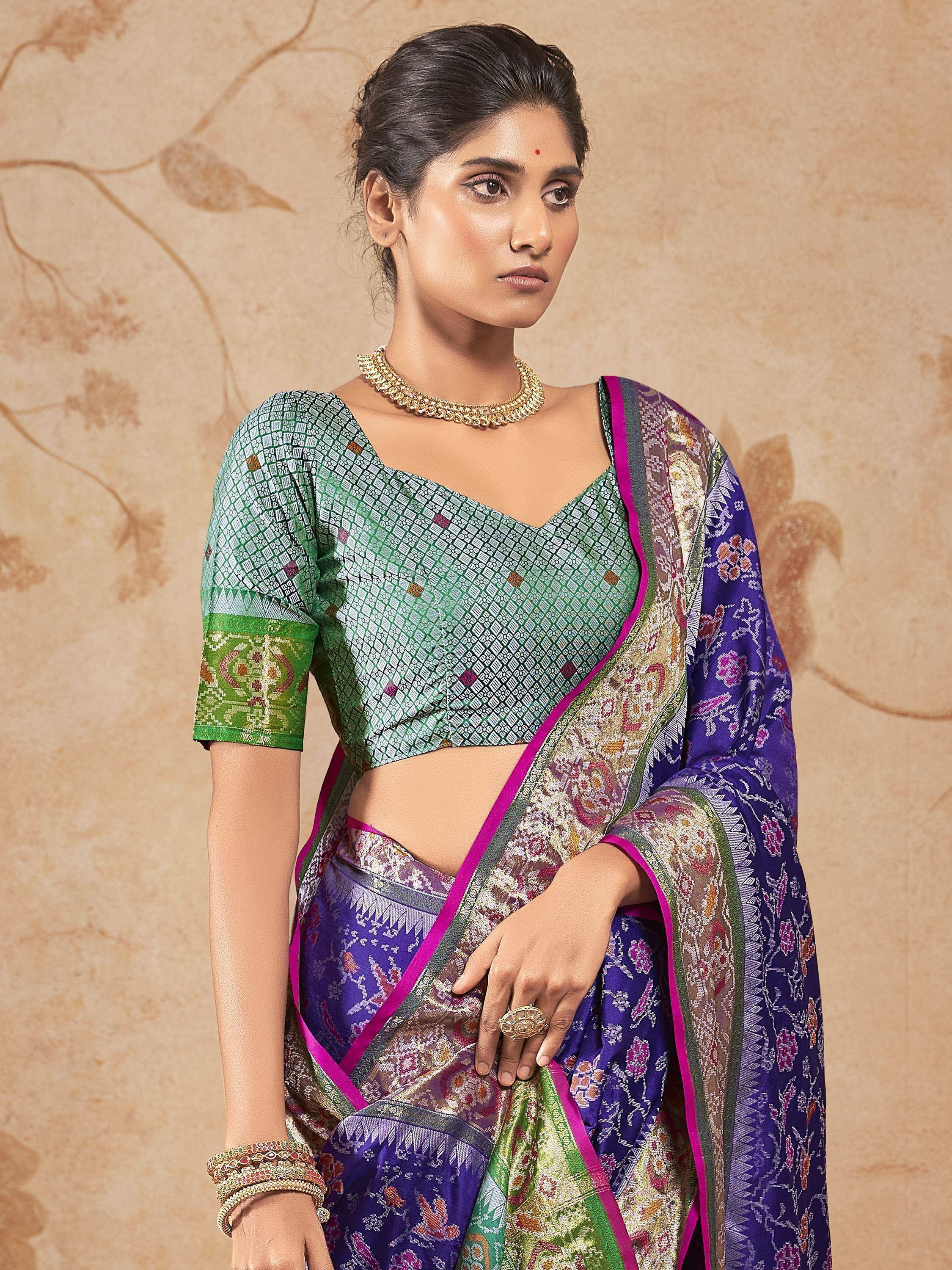 Woman in purple and green designer saree with intricate patterns and gold jewelry, ethnic wear