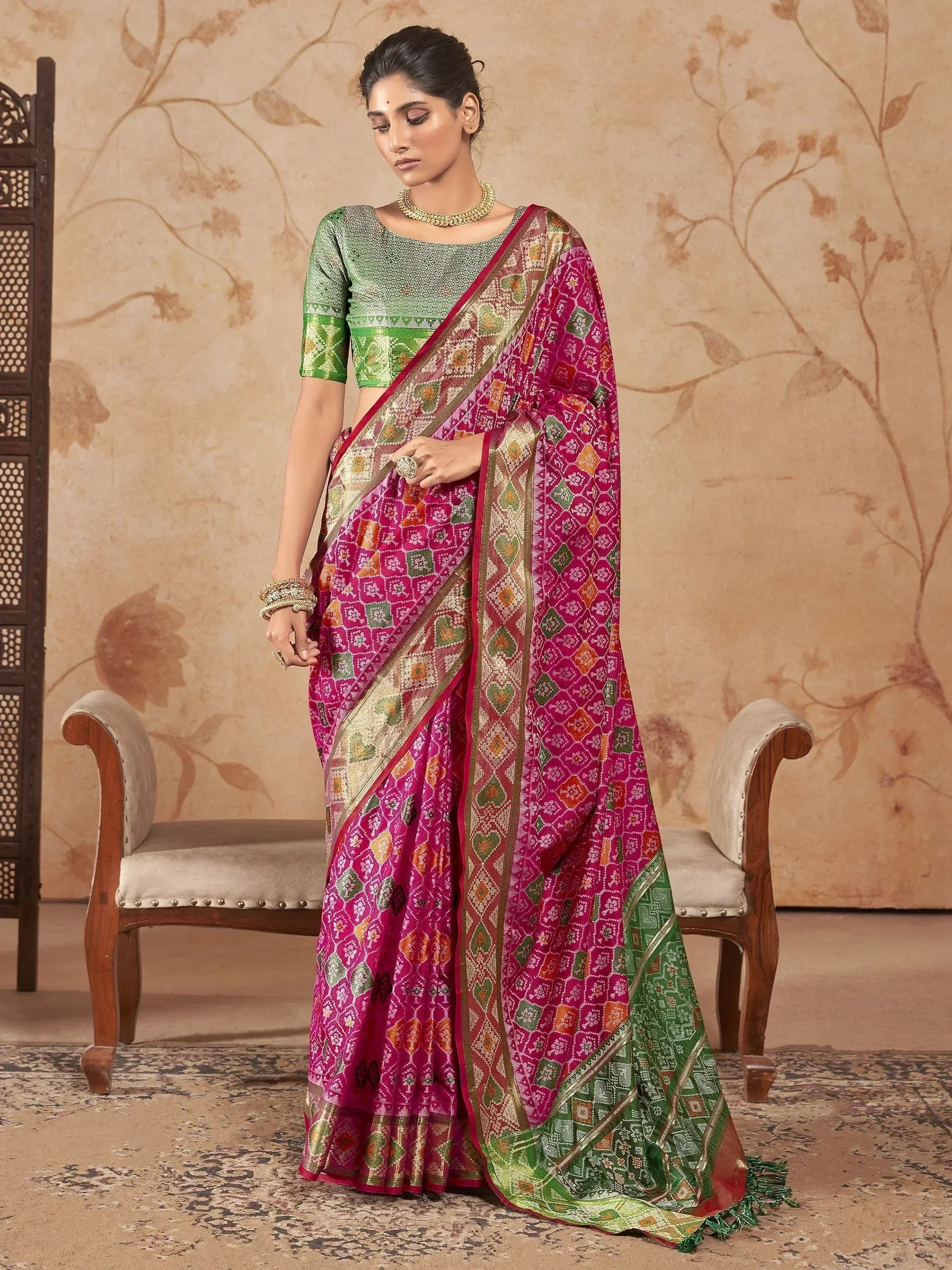Woman in vibrant pink and green ethnic saree with intricate geometric patterns, perfect for festive occasions.