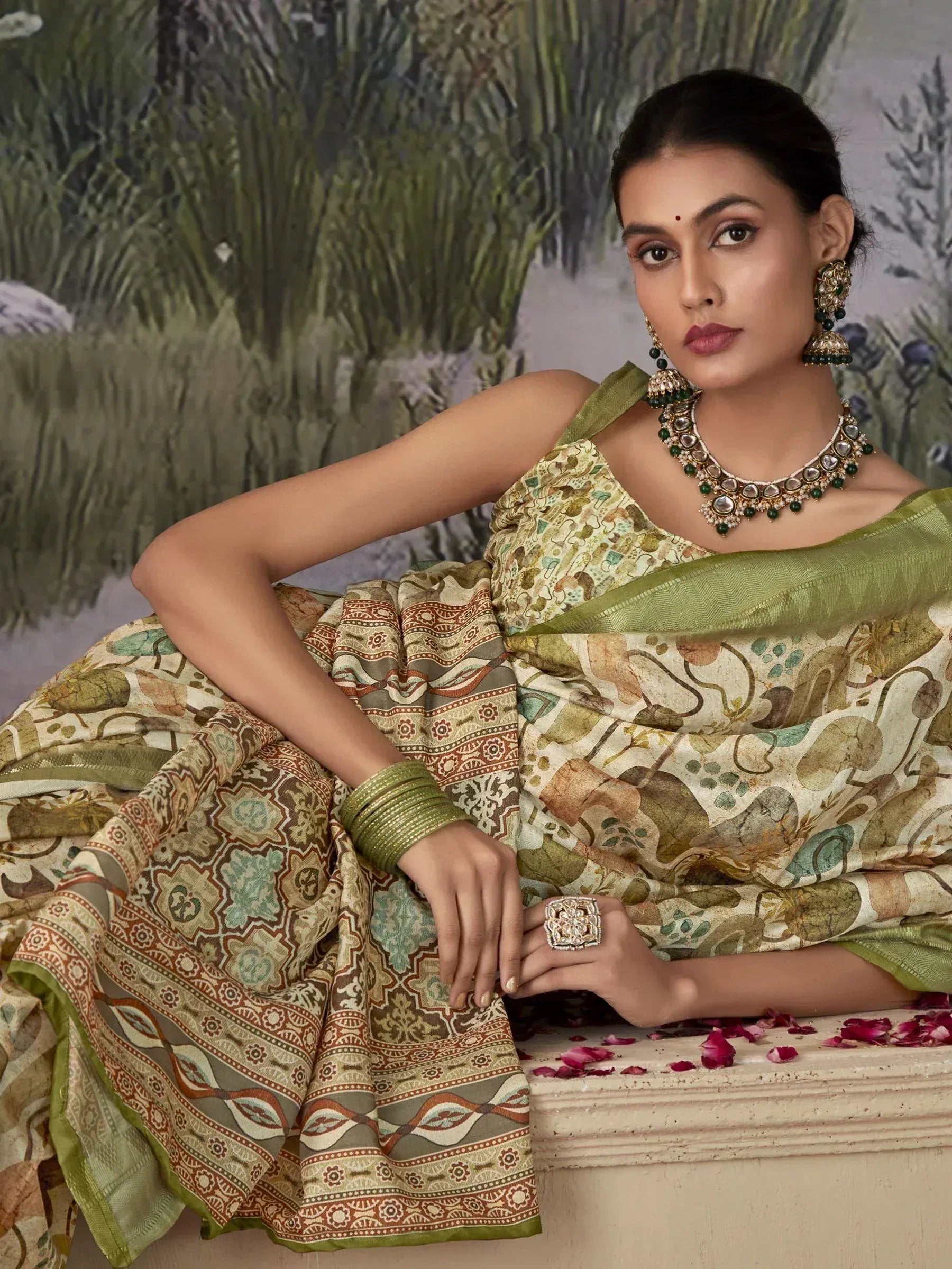 Woman in elegant printed saree with green border, traditional jewelry, and rose petals, showcasing Indian ethnic wear.