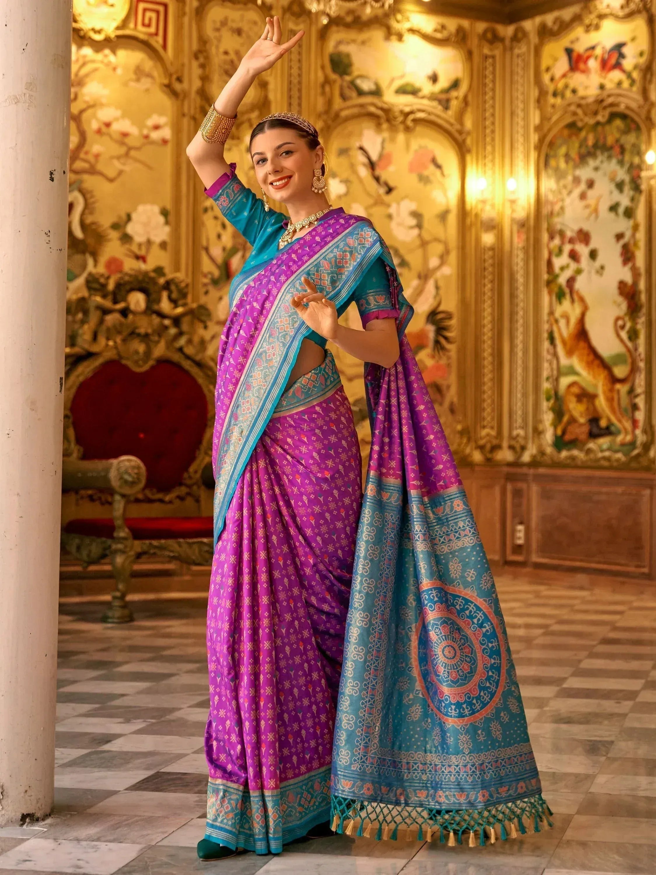 Woman in vibrant purple and blue printed saree with gold jewelry, posing elegantly in ornate palace setting
