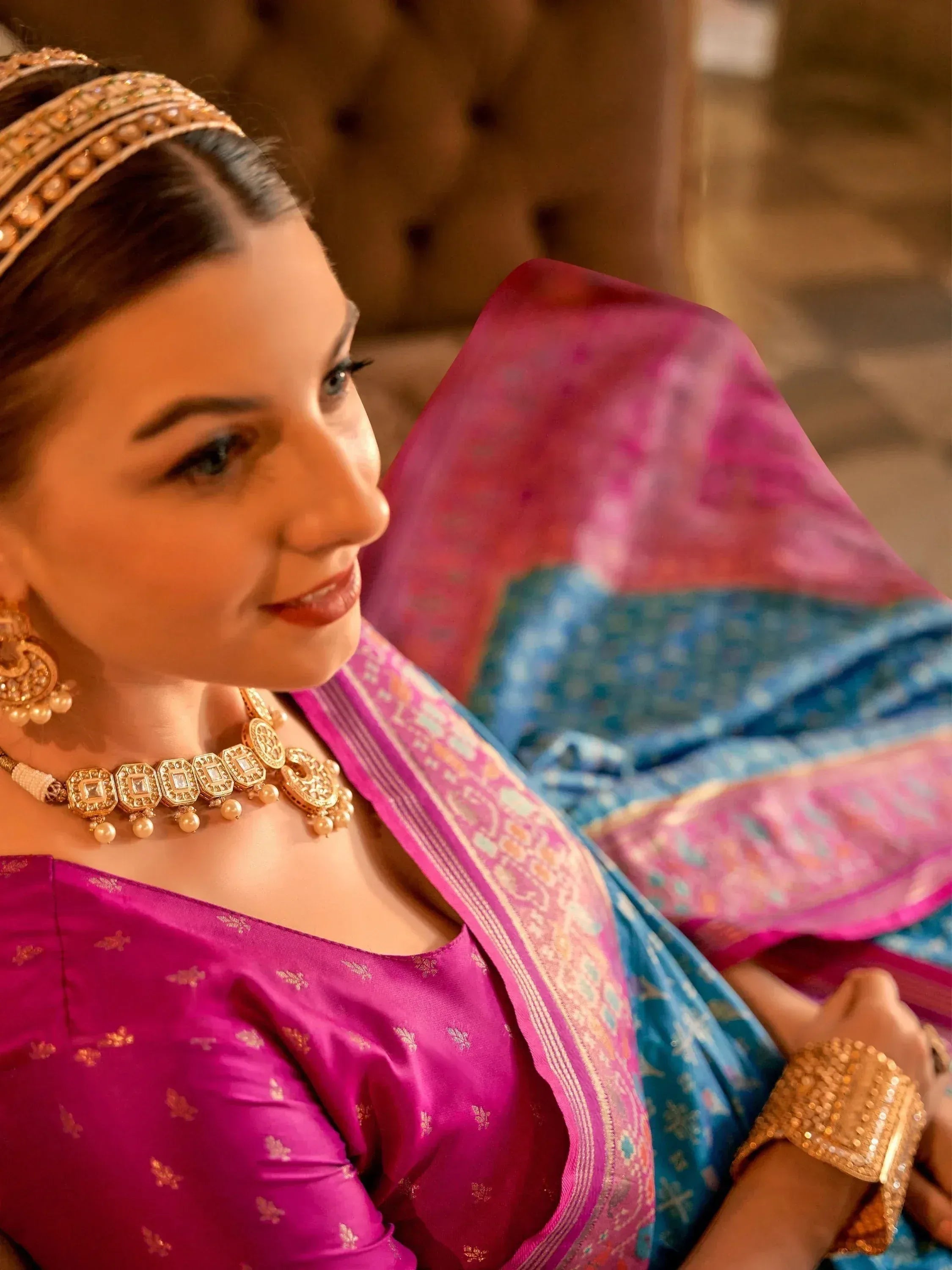 Woman in vibrant pink and blue Indian saree with gold jewelry, showcasing ethnic wear