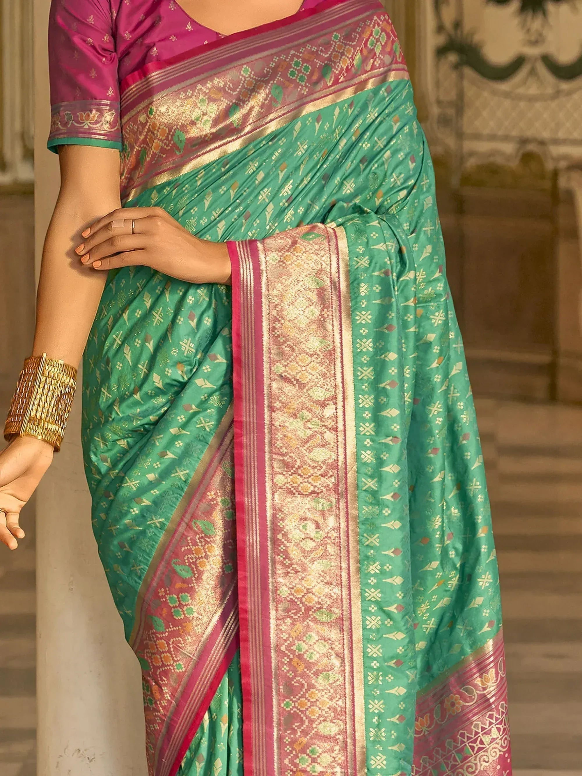 Green and pink designer saree with intricate gold patterns and embroidered border, paired with matching blouse.
