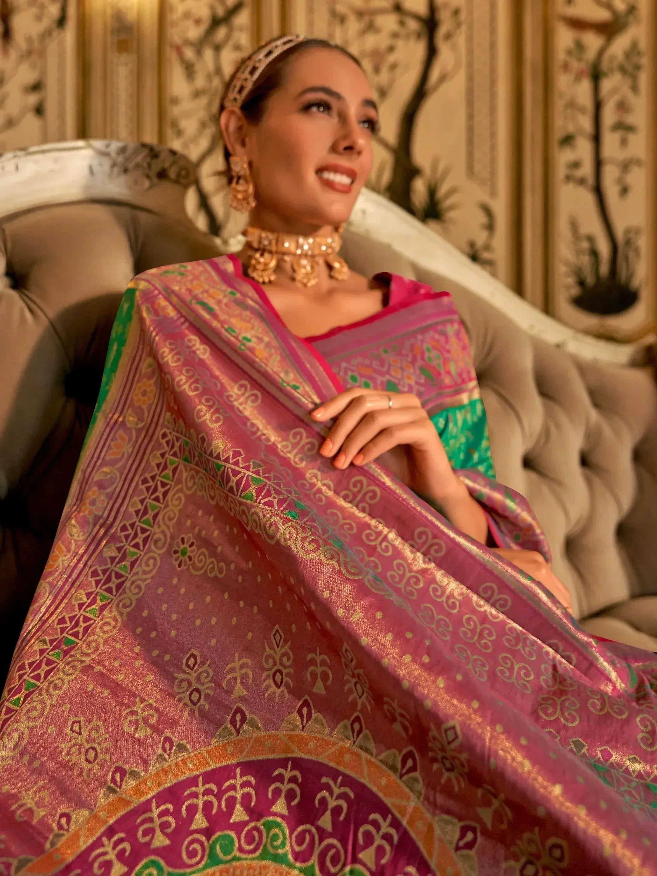 Woman in vibrant pink and green ethnic saree with gold embroidery, styled with traditional jewelry for festive occasions.