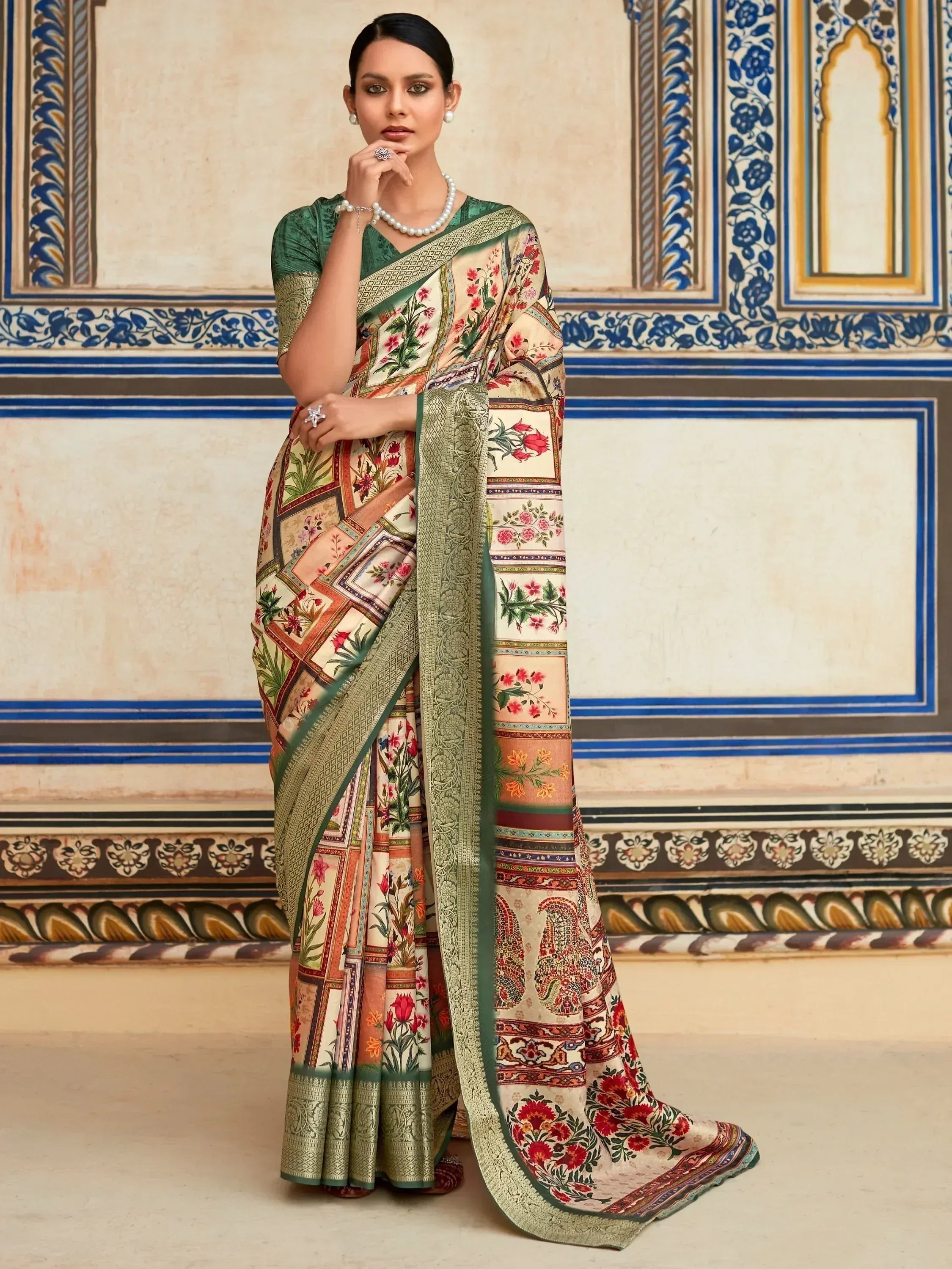 Elegant floral print saree with green border, styled with pearl jewelry against ornate Indian wall backdrop